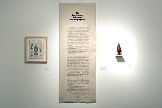 A long piece of paper is hanging on a wall next to a picture and a vase