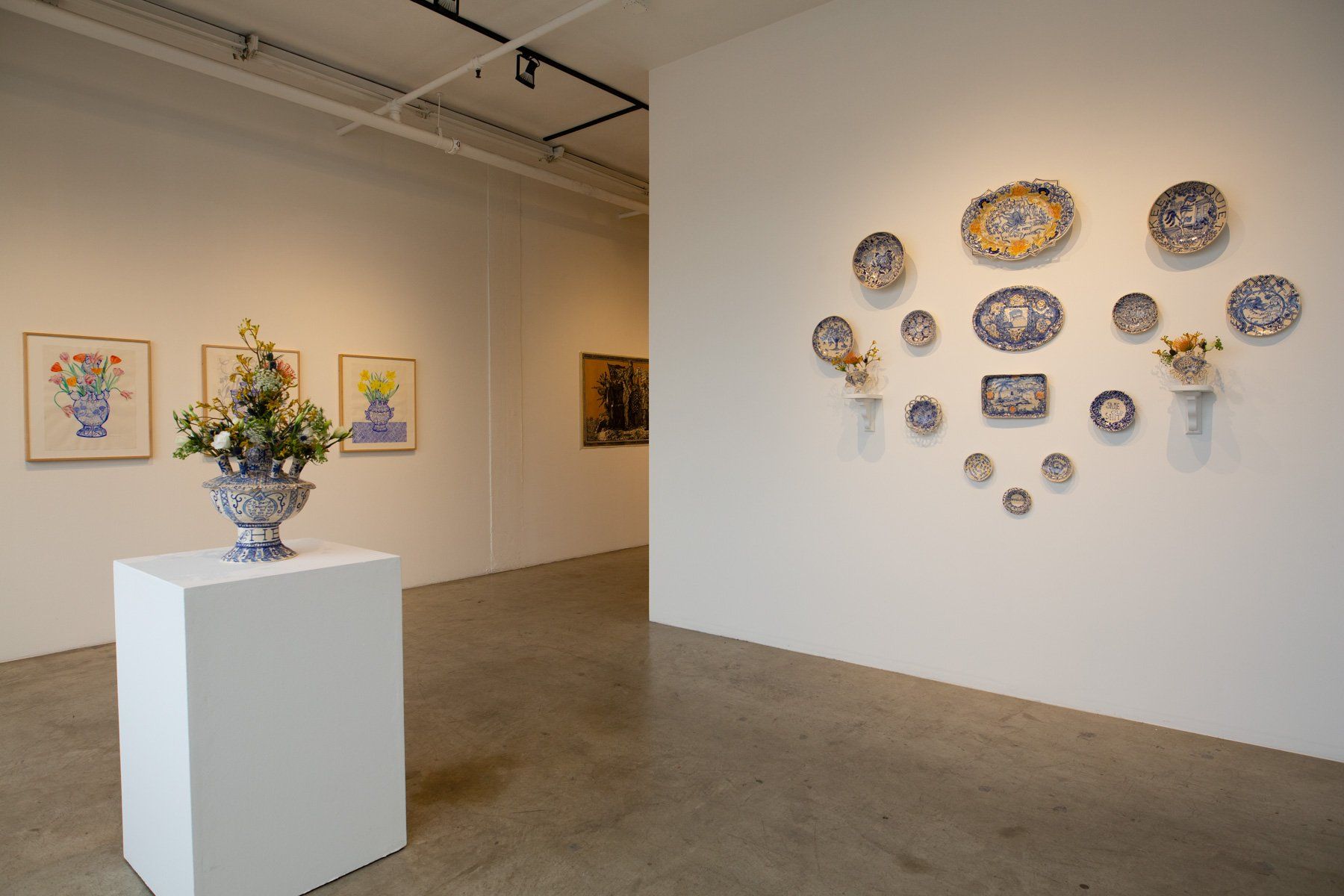 A vase of flowers is on a pedestal in a room with plates on the wall.