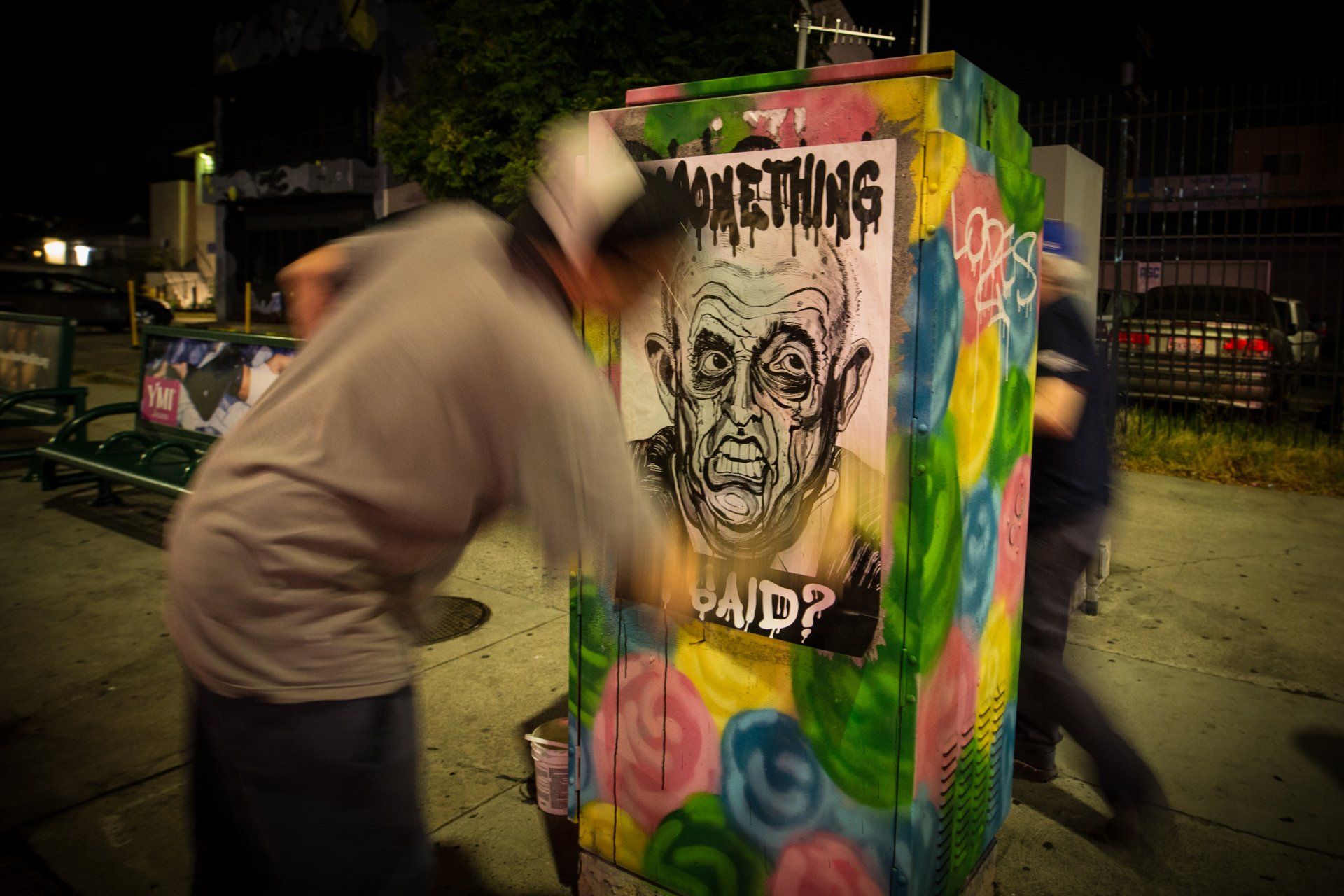 A man is spray painting a picture of an old man on a box.