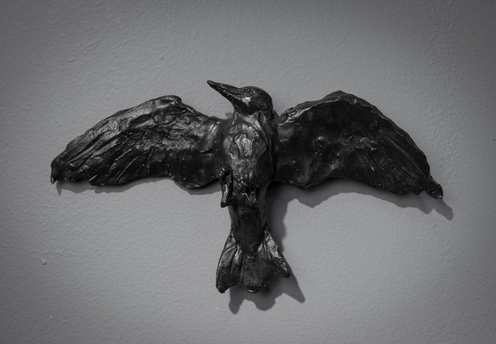 A black and white photo of a statue of a bird flying on a wall.