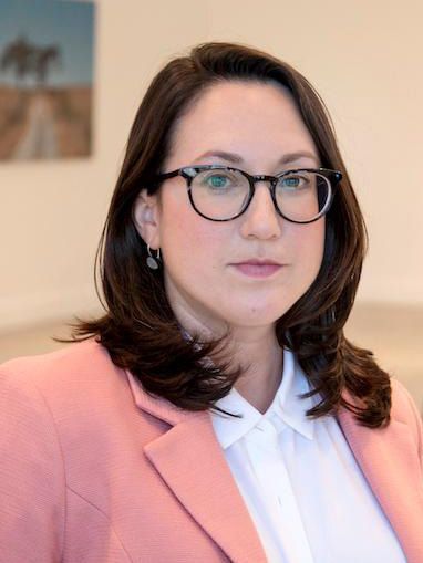 A woman wearing glasses and a pink jacket is looking at the camera.