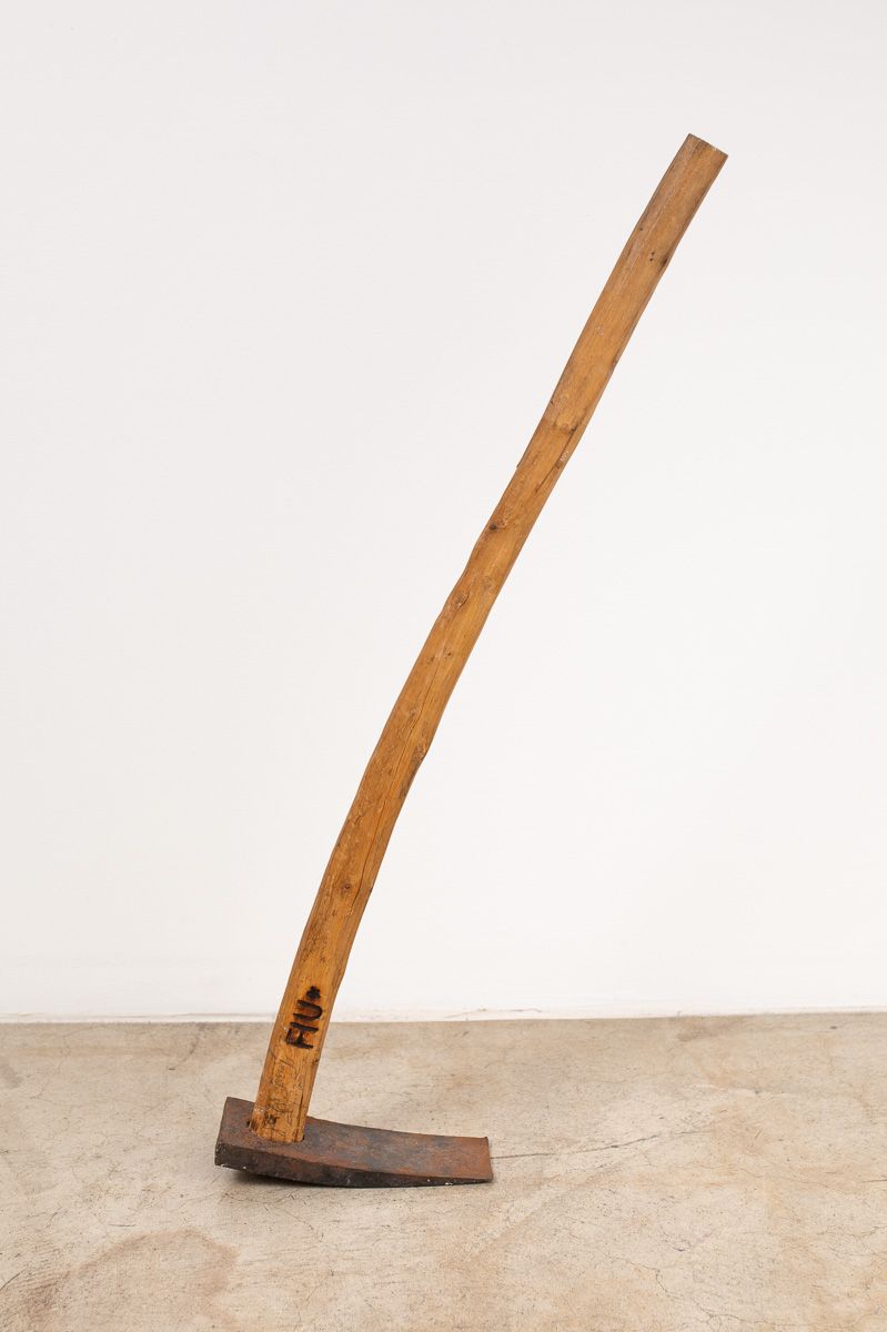 An old hoe with a wooden handle is sitting on a concrete surface.