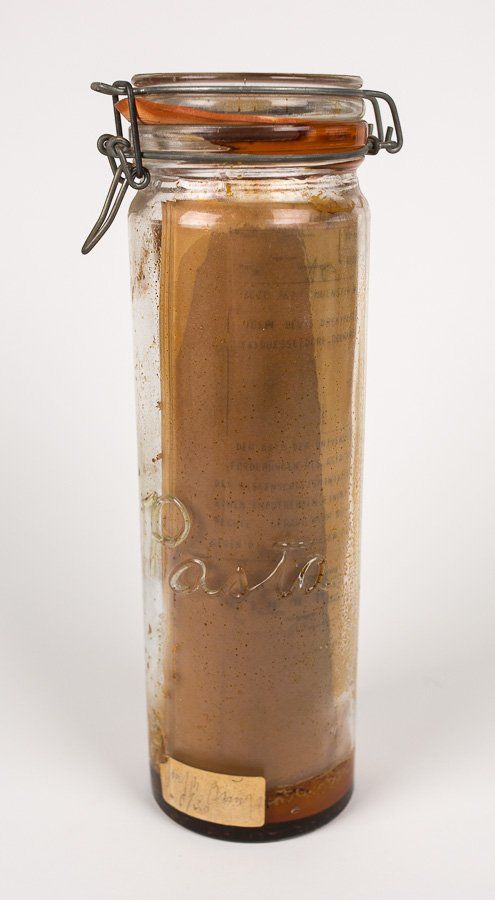 A glass jar filled with brown liquid is sitting on a white surface.