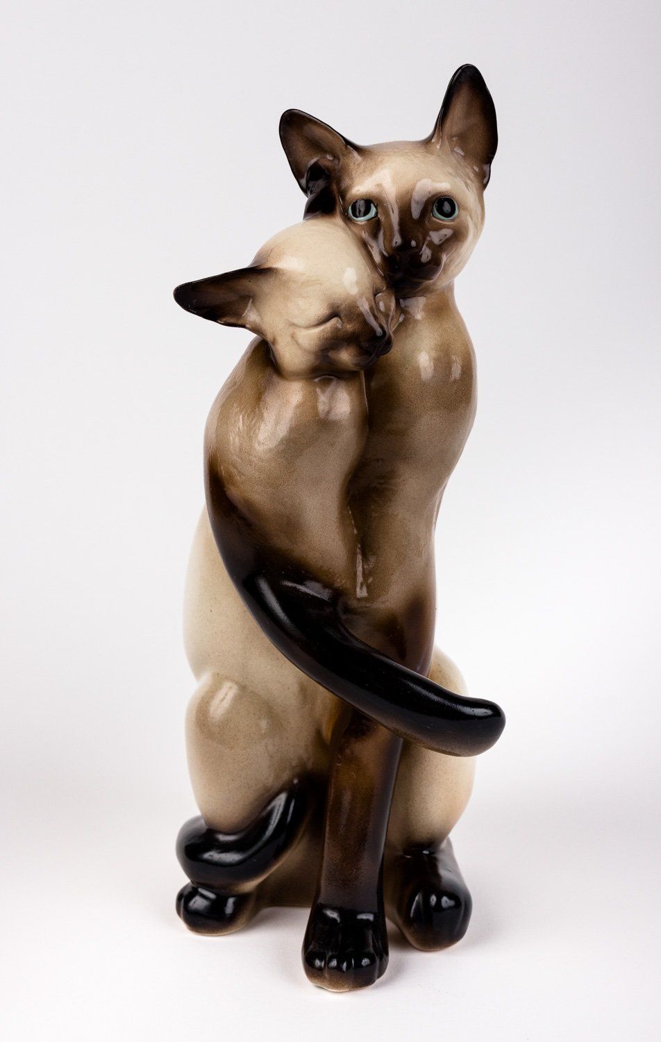 A statue of two siamese cats hugging each other on a white background.