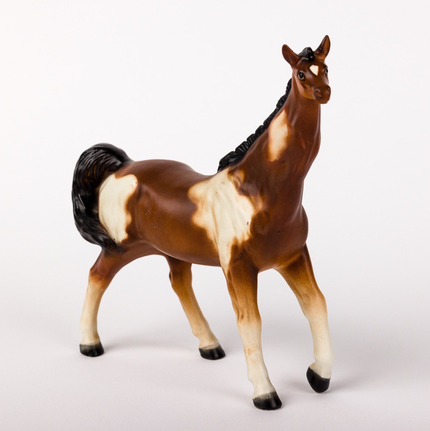 A brown and white horse figurine is standing on a white surface