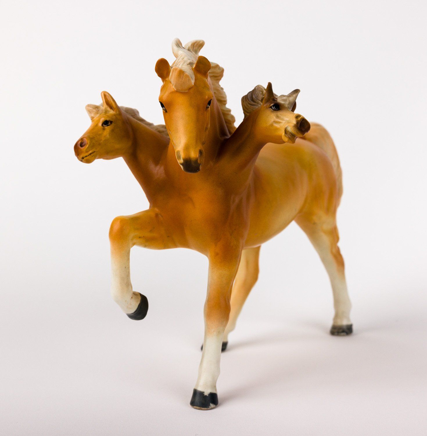 A toy horse with three heads is standing on its hind legs
