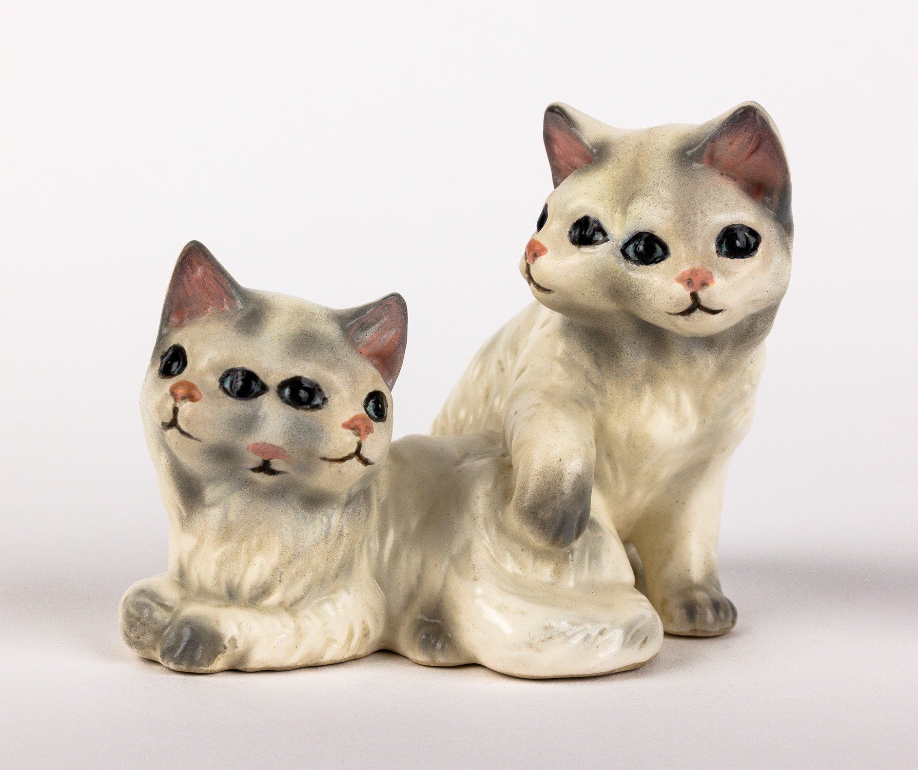 Two ceramic cats are sitting next to each other on a white surface
