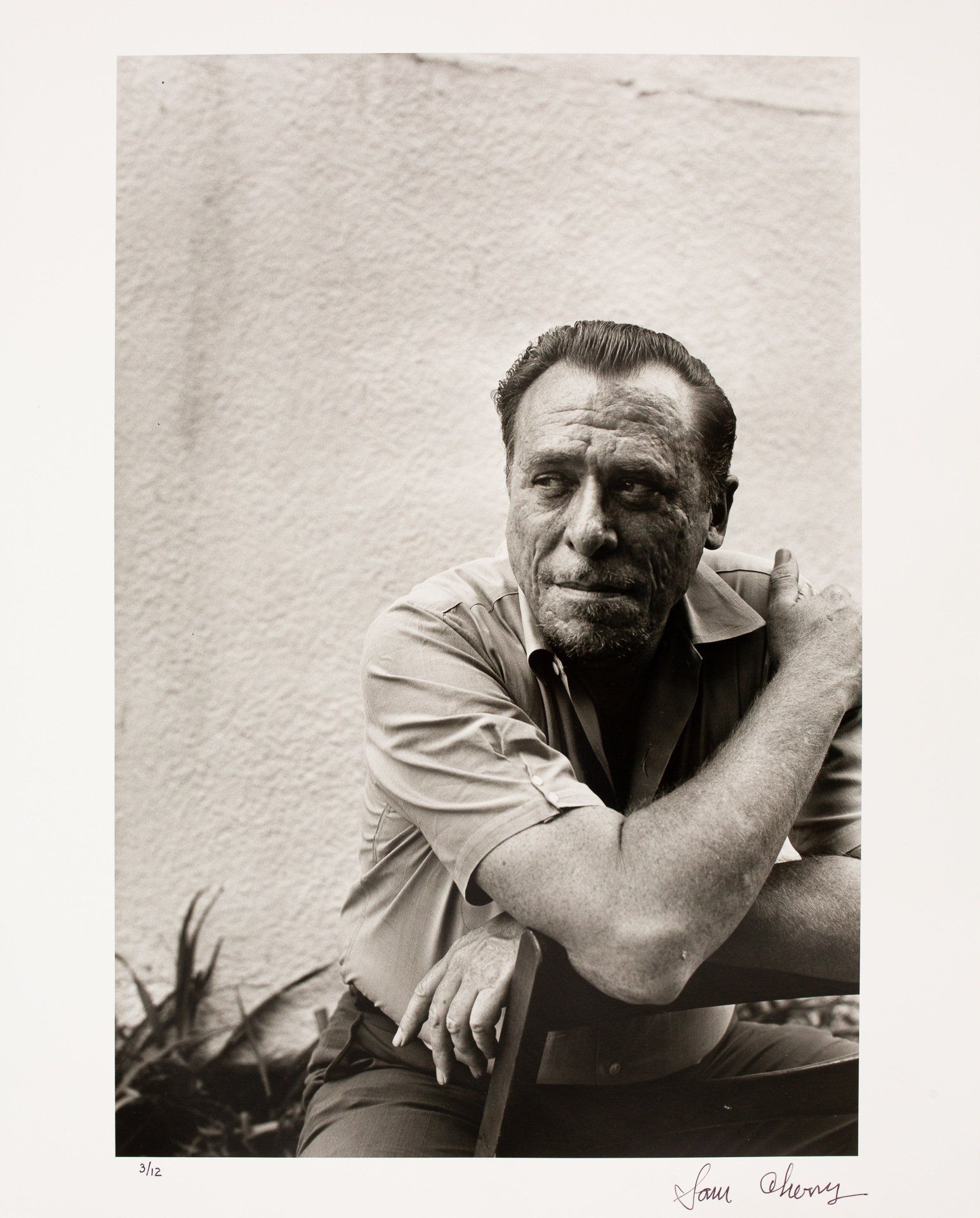 A black and white photo of a man leaning on a chair.