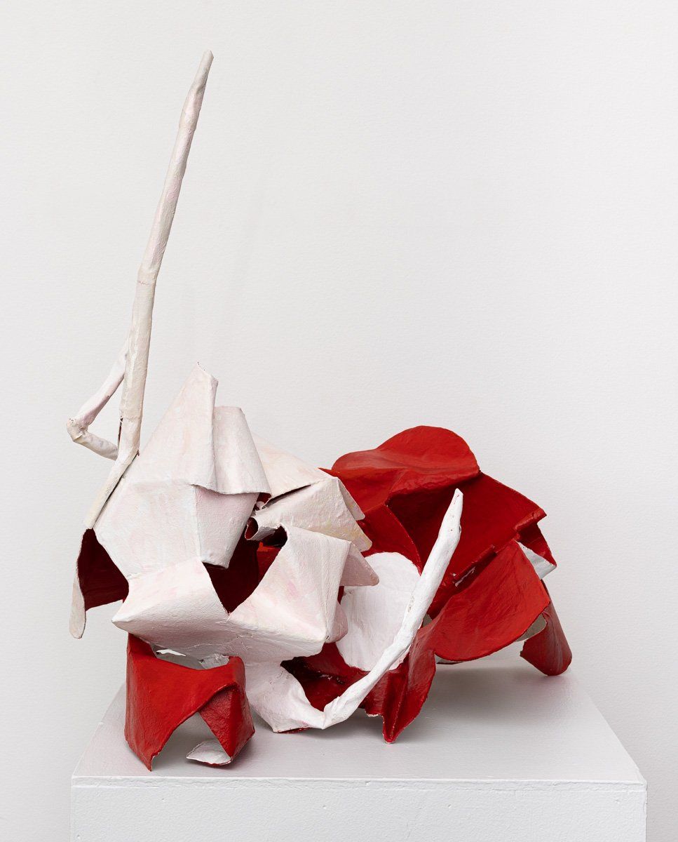 A red and white sculpture is sitting on a white cube