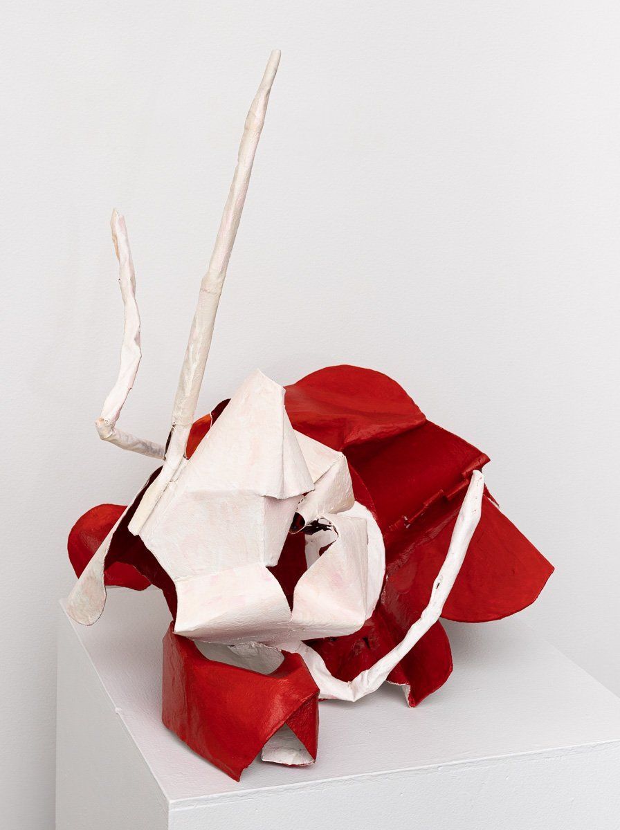 A white and red sculpture is sitting on a white cube