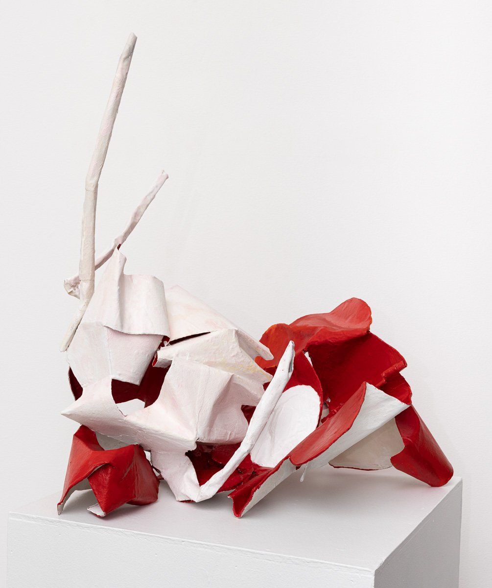 A red and white sculpture is sitting on a white cube