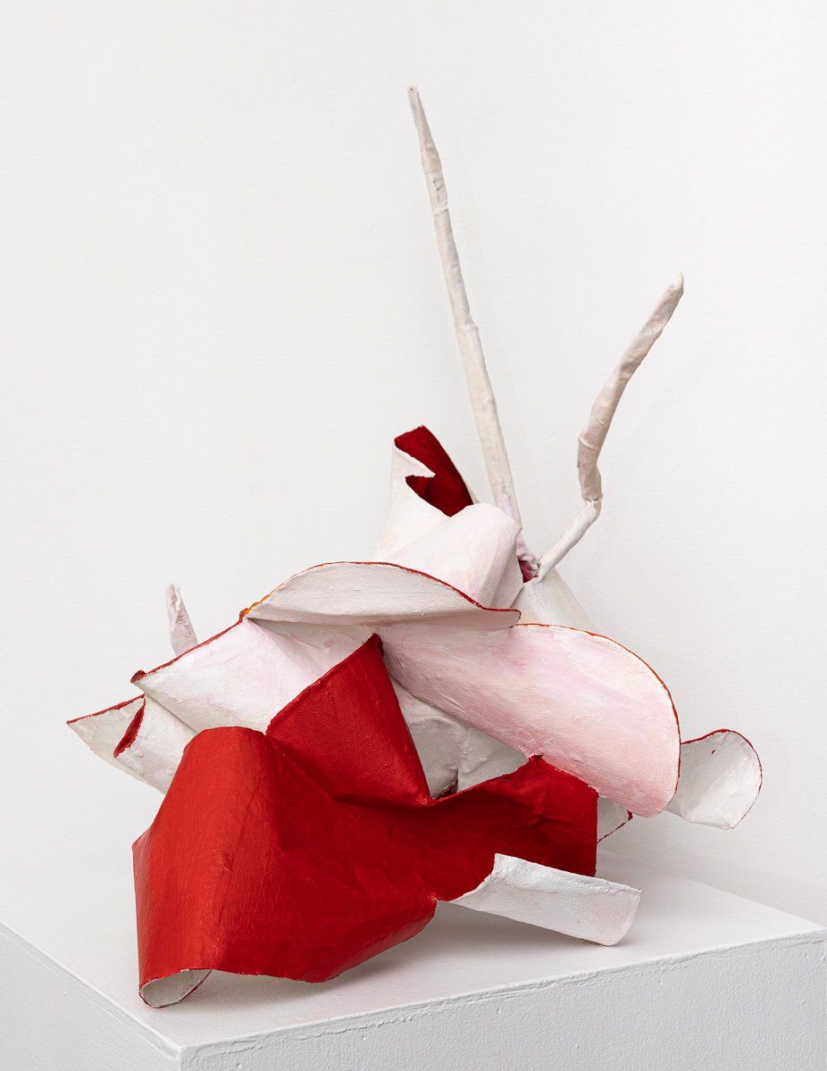 A red and white sculpture is sitting on a white cube