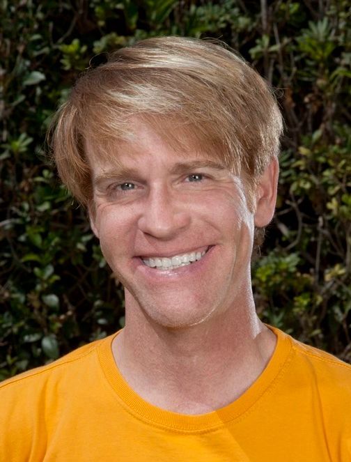 A man wearing a yellow shirt is smiling for the camera.