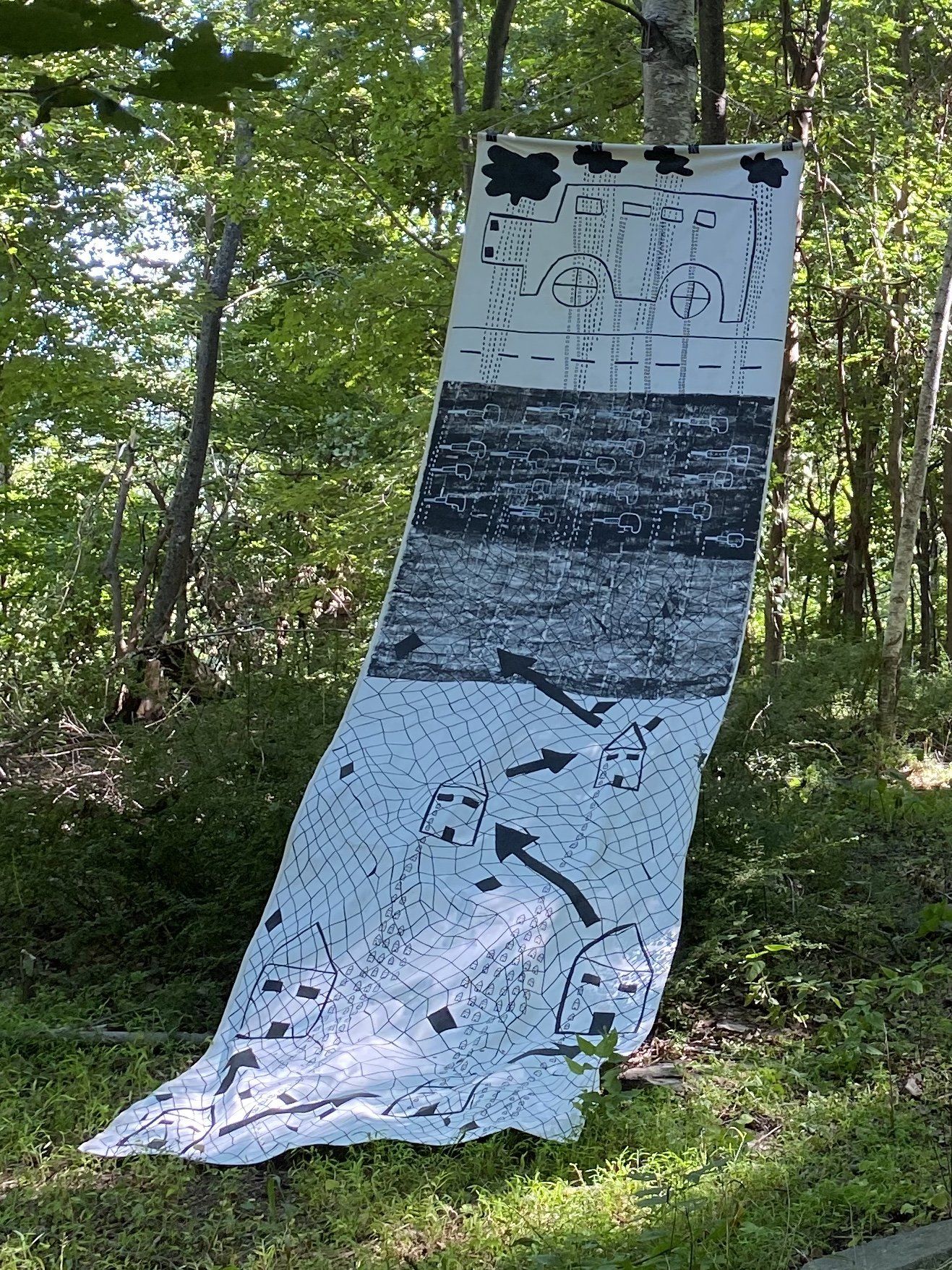 A large piece of art is hanging from a tree in the woods.