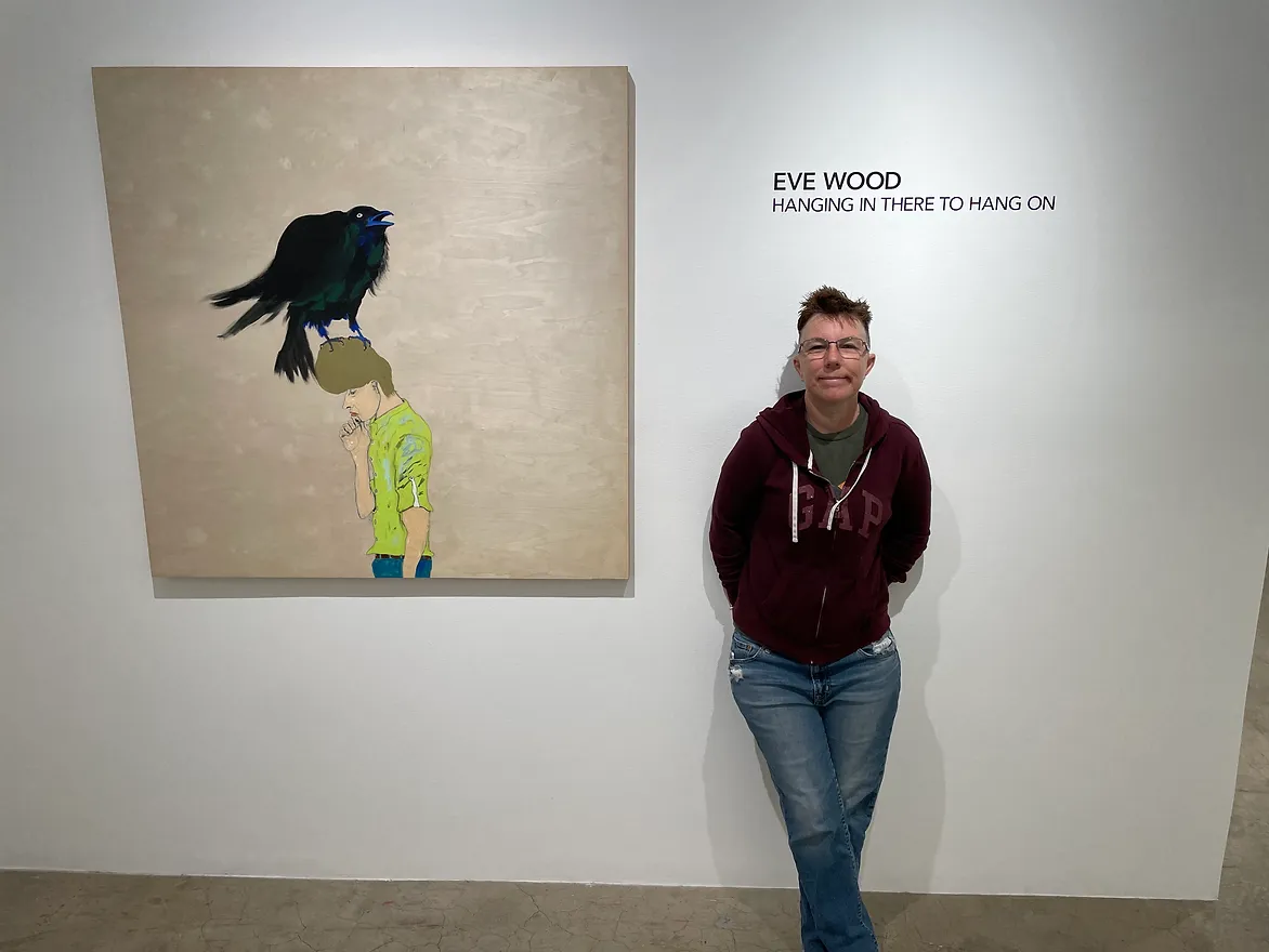 A woman is standing next to a painting of a bird on a child 's head.