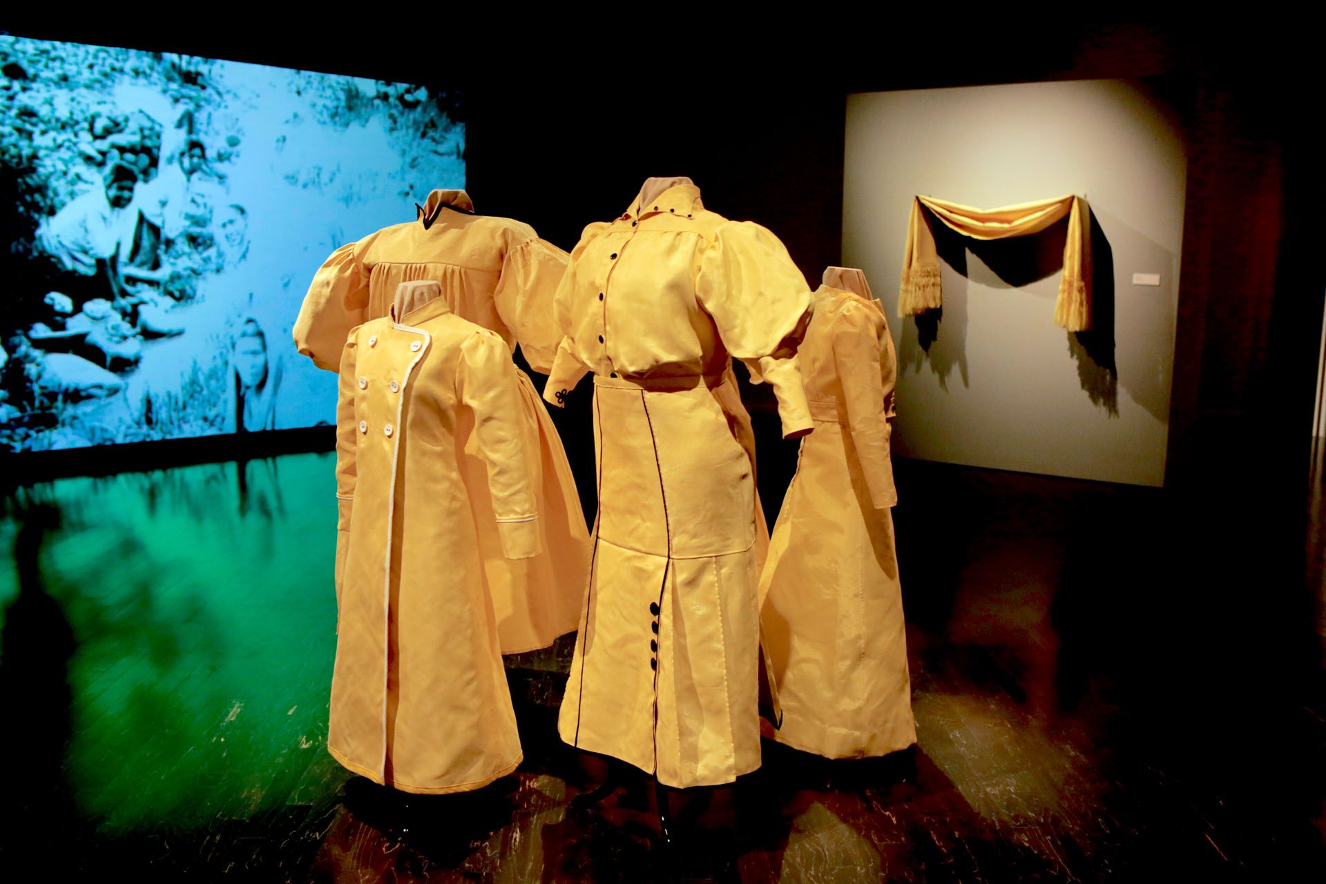 A group of yellow dresses are on display in a dark room