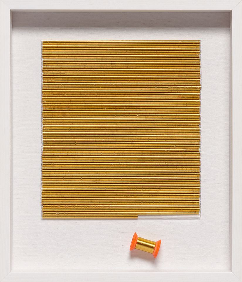 A picture of a square made of wooden sticks and an orange spool of thread.