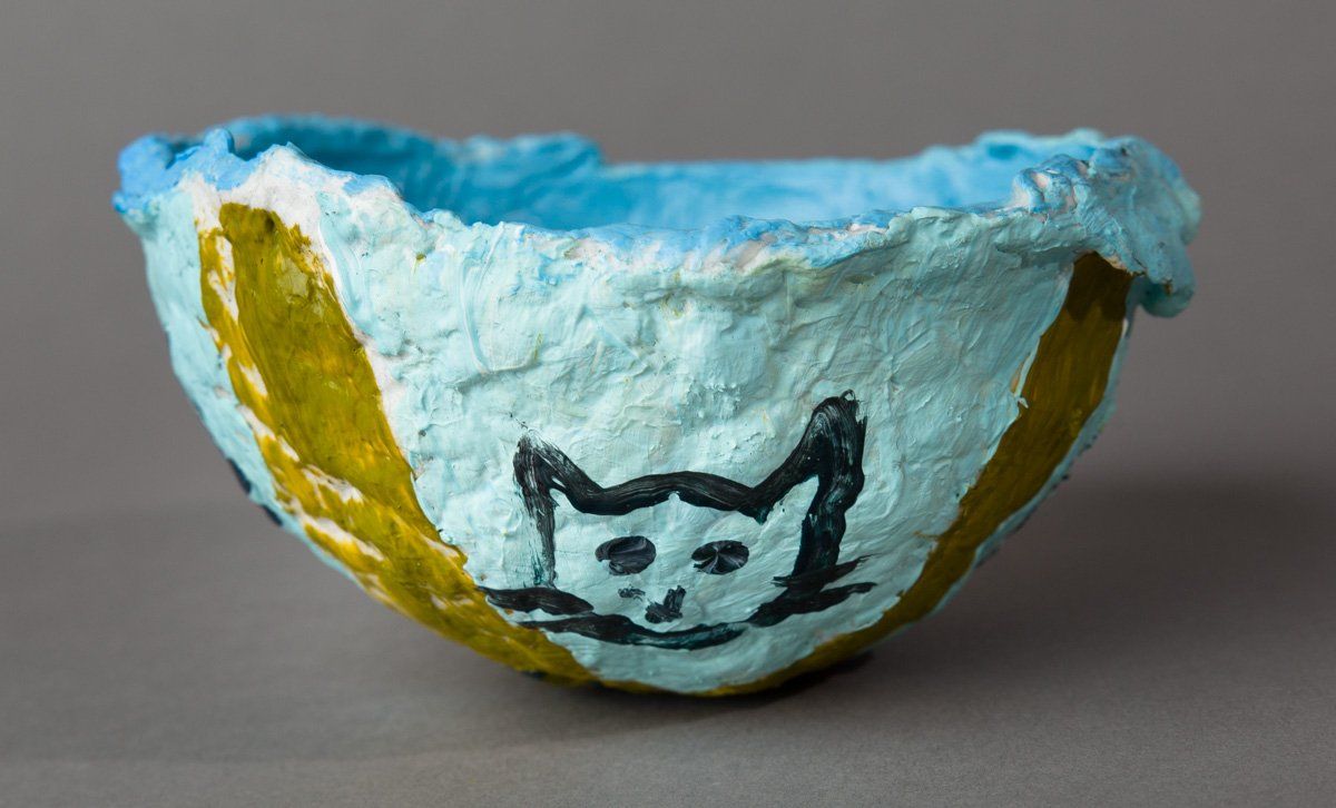 A blue and yellow bowl with a cat face painted on it.