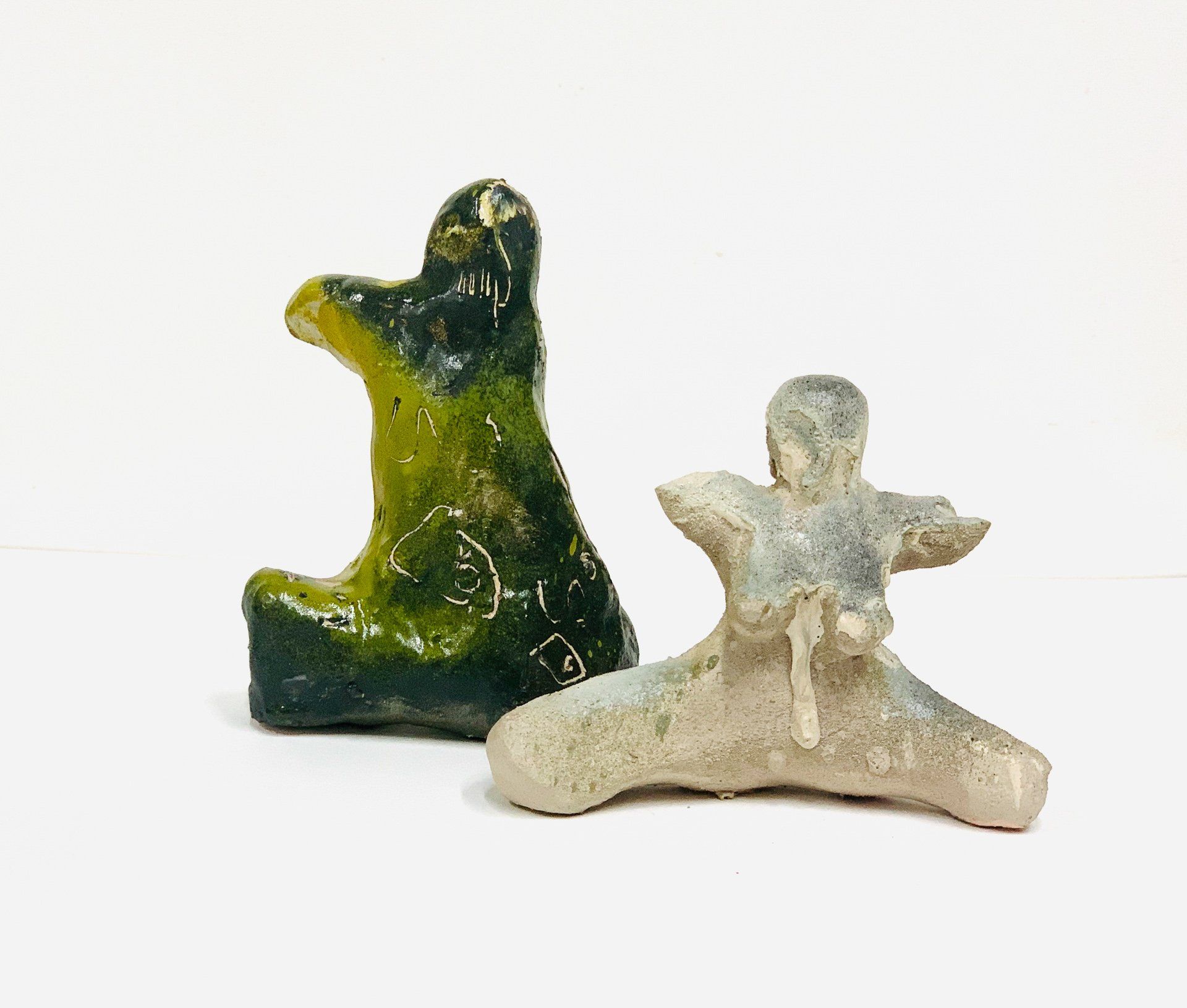 Two ceramic figurines are sitting next to each other on a white surface.