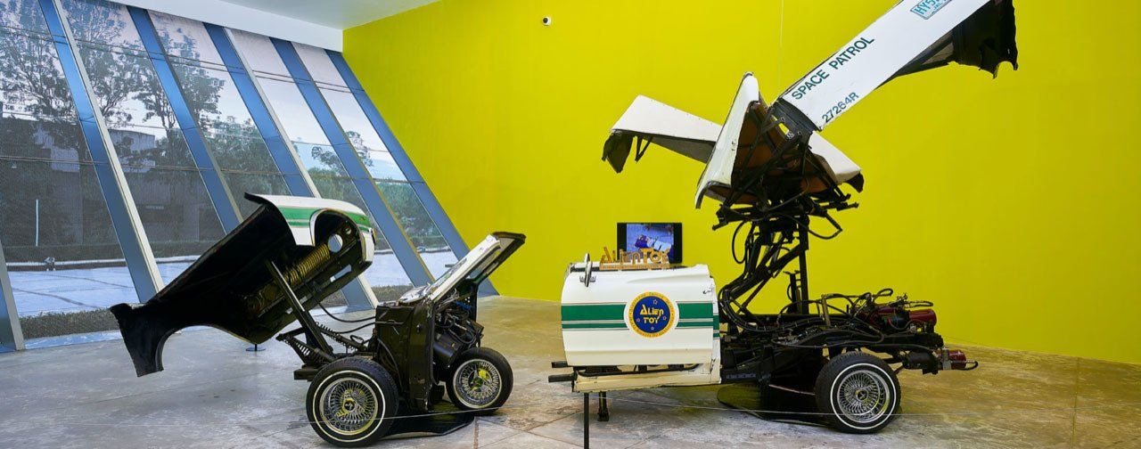 Two robots are sitting next to each other in a room with a yellow wall.