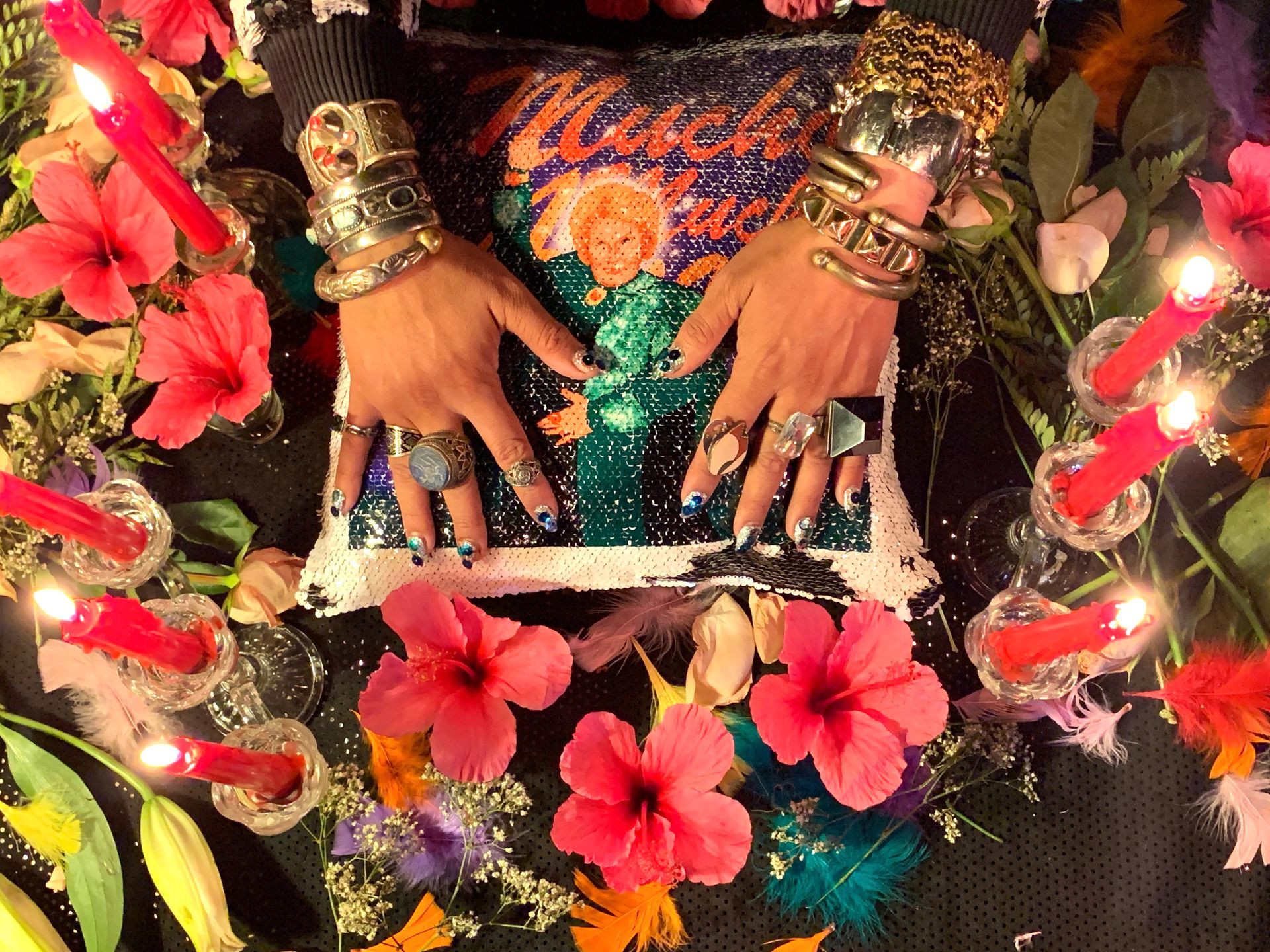 Jeweled hands on top of a pillow surrounded by a ring of flowers and candles.
