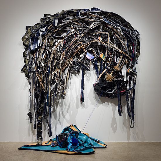 A sculpture made out of a bunch of objects is hanging on a wall.
