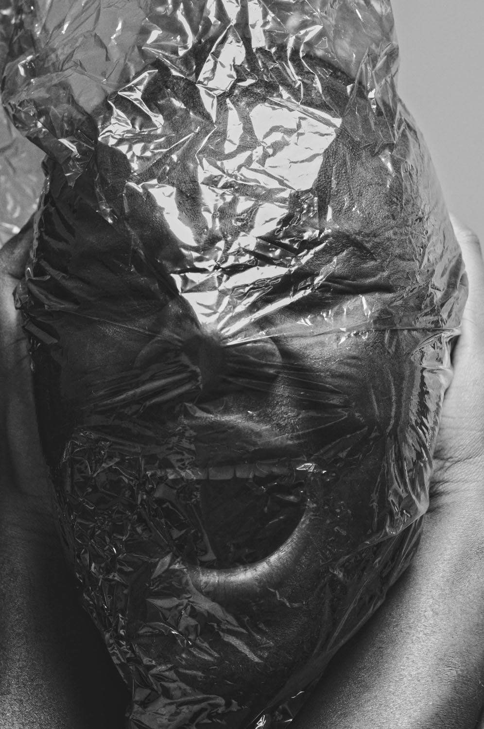 A black and white photo of a person 's face wrapped in plastic.