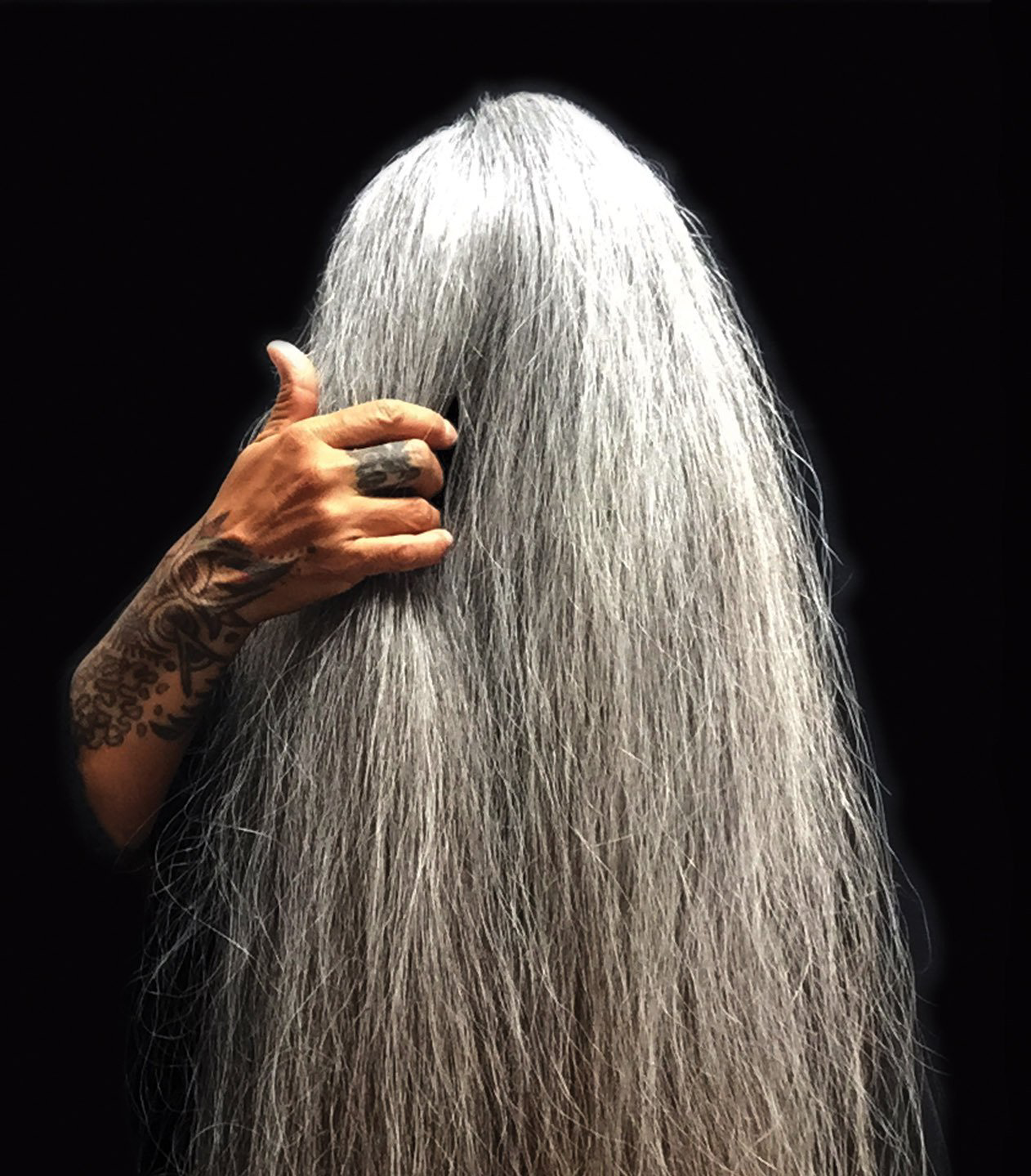 A woman with very long gray hair is covering her face with her hand.
