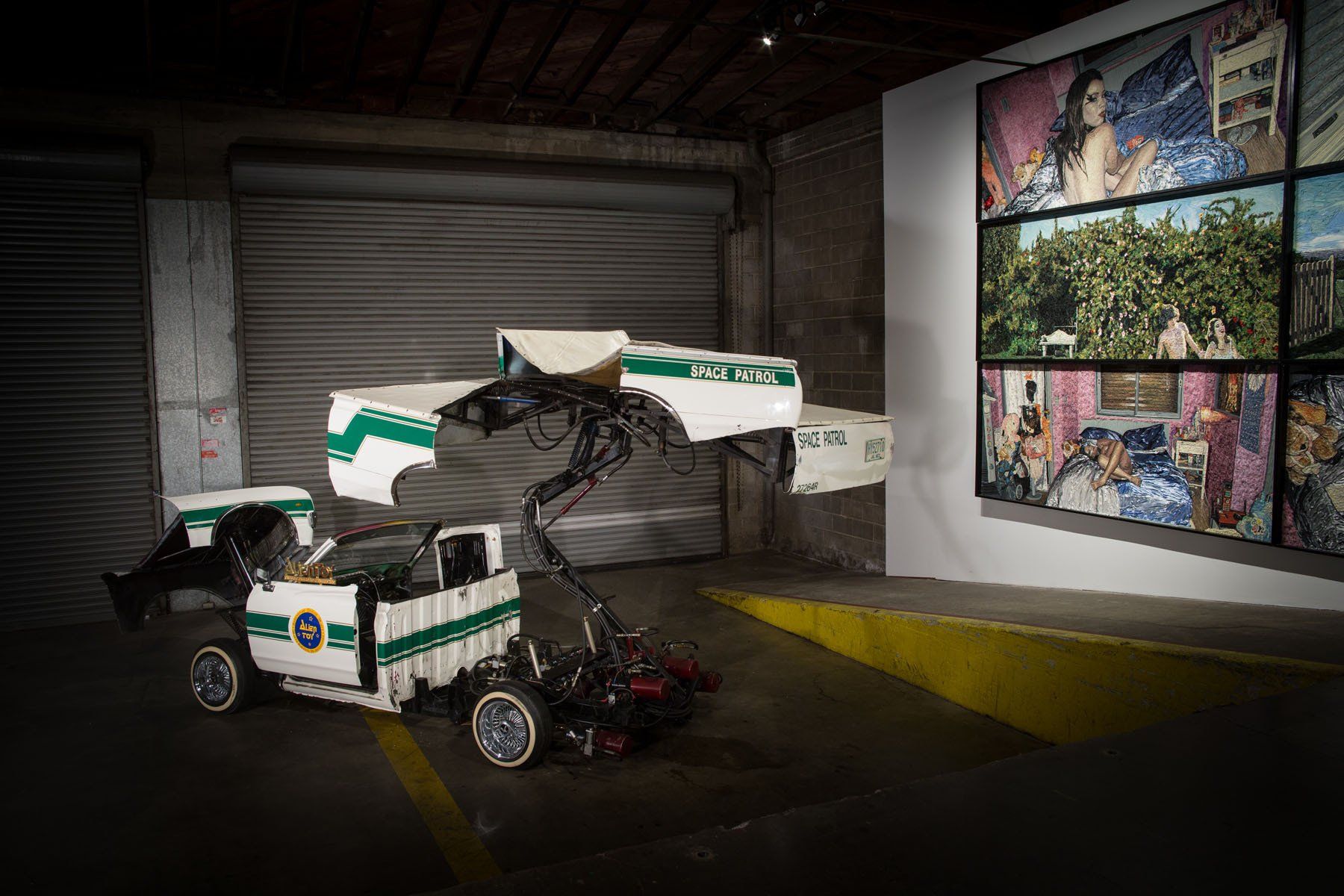A white and green truck is parked in a garage next to a painting on a wall.