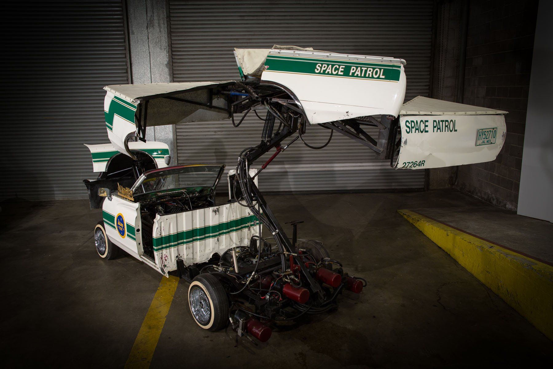 A white and green space patrol car is parked in a garage.