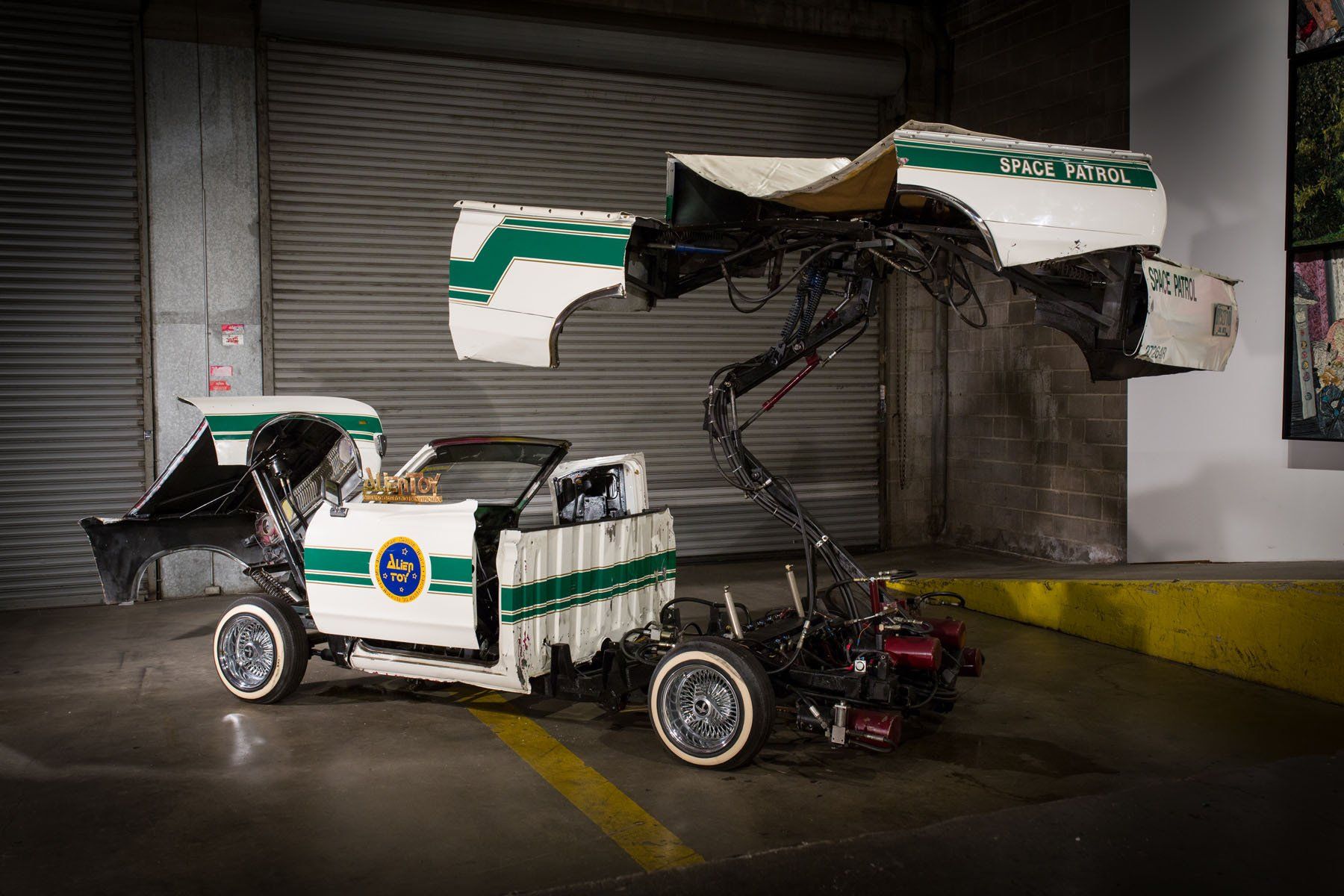 A white and green police car is being dismantled in a garage.