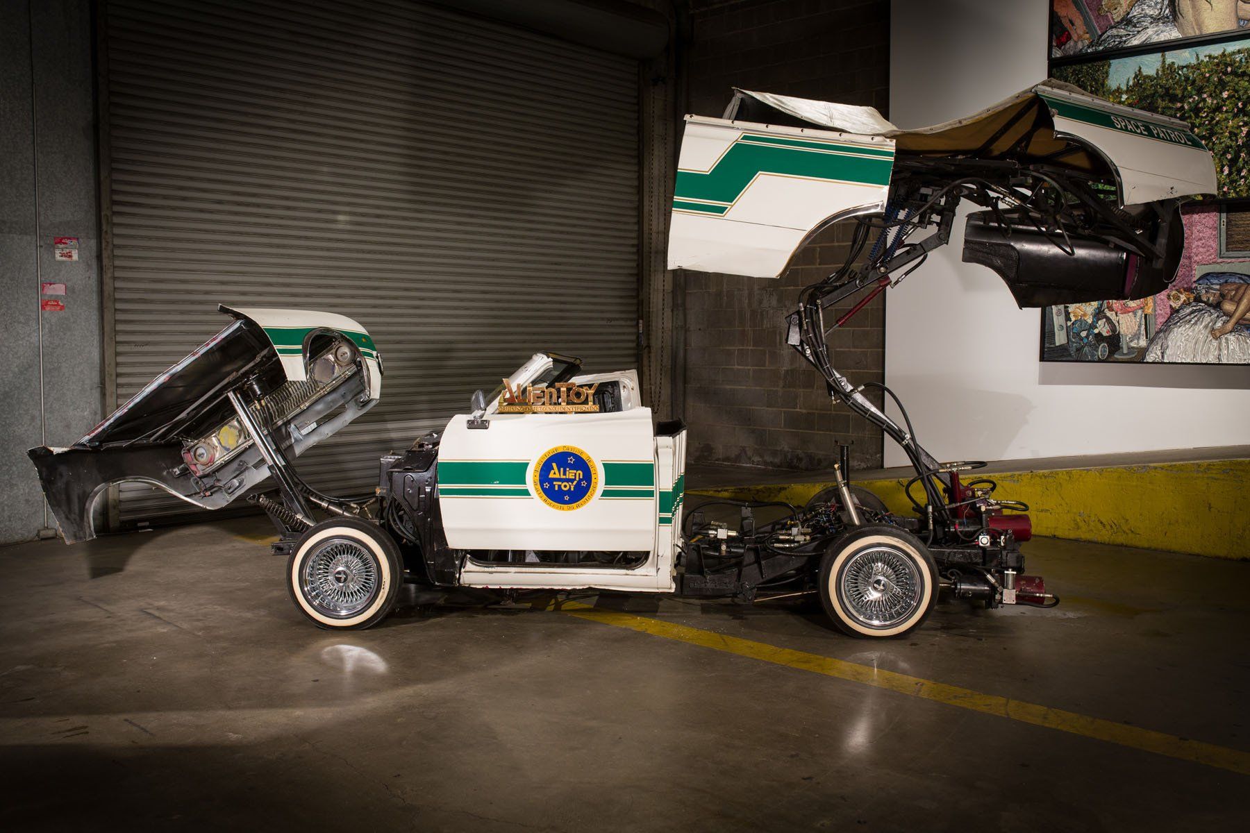 A white and green police car is parked in a garage with its doors open.