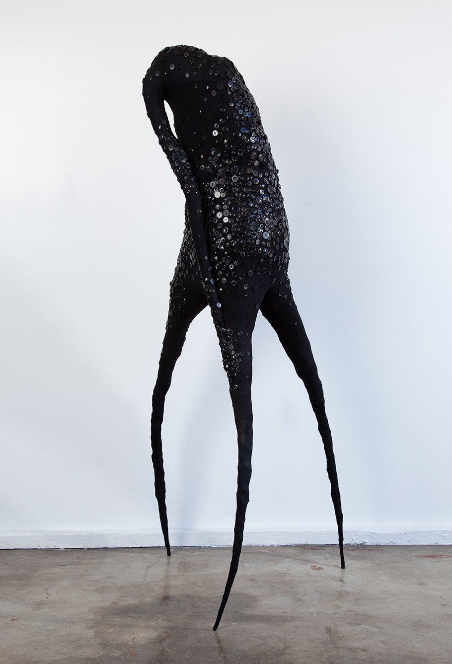 A black sculpture with long legs is standing in front of a white wall