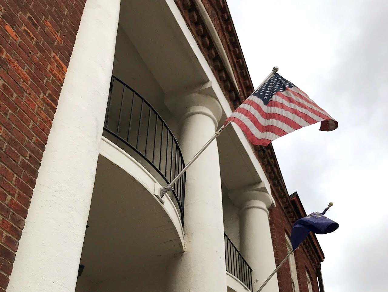 American flag and blue flag on building with white columns and red brick facade.