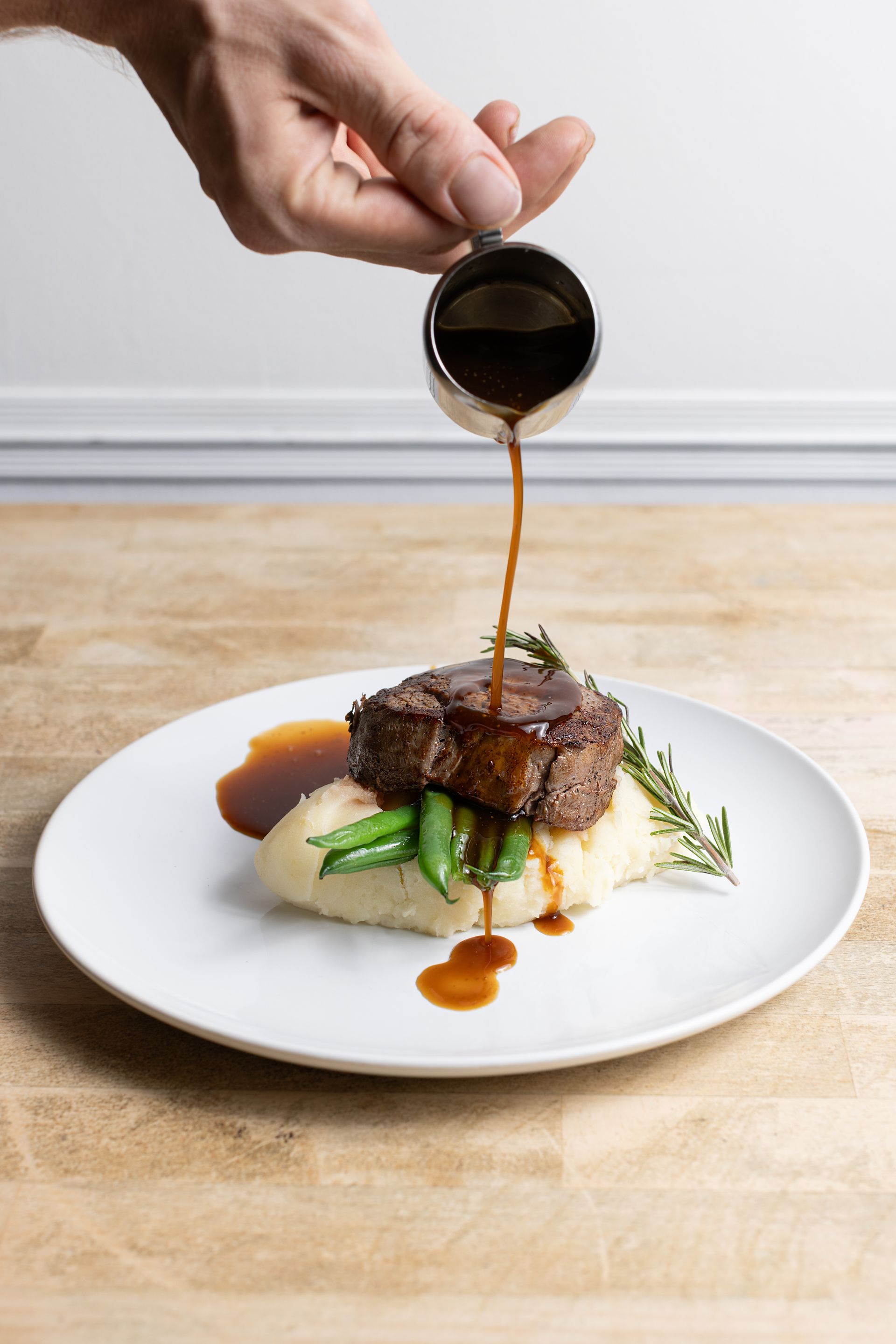 A person is pouring sauce on a plate of food.