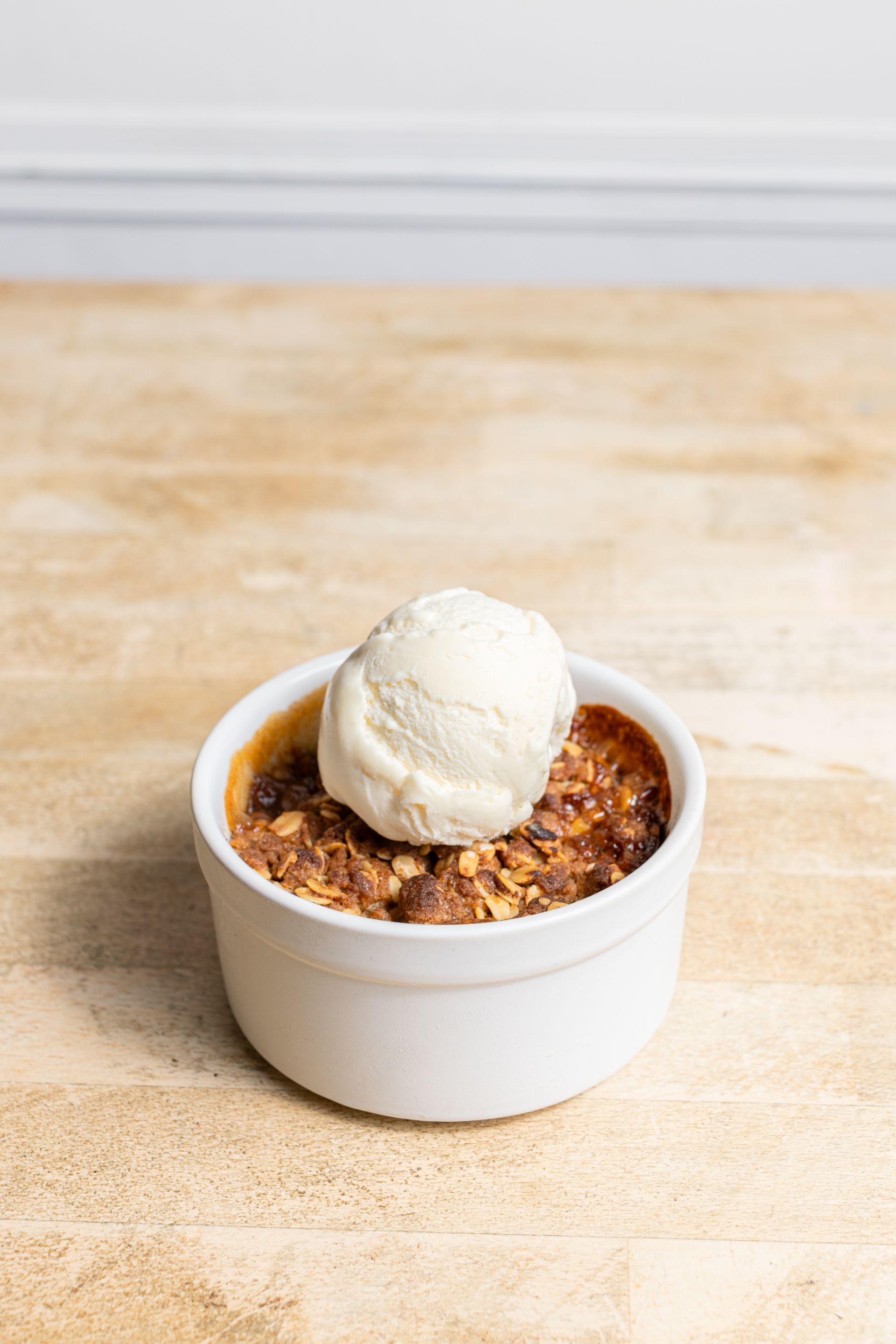 A bowl of food with ice cream on top of it on a wooden table.