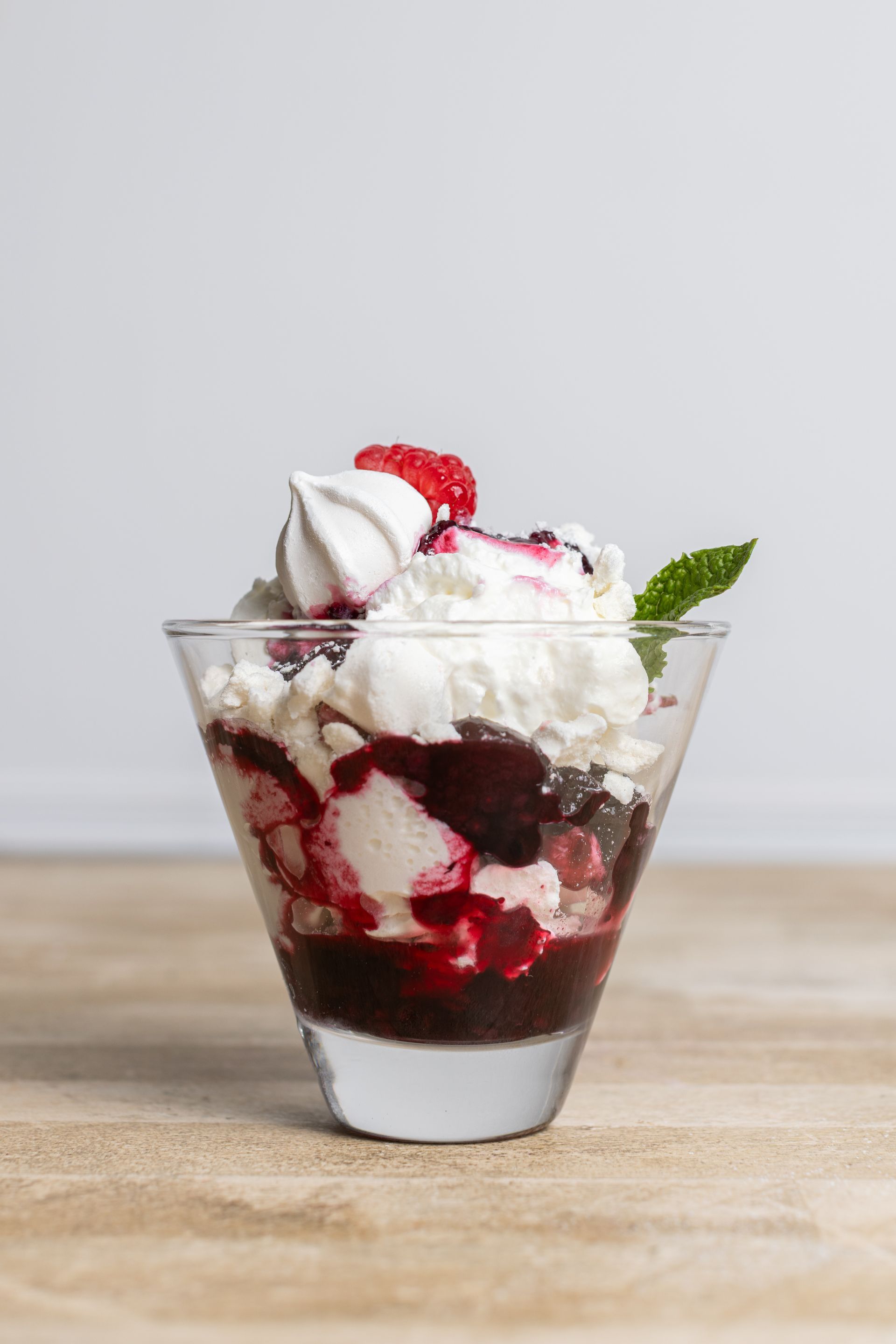 A glass of ice cream with whipped cream and berries on a wooden table.
