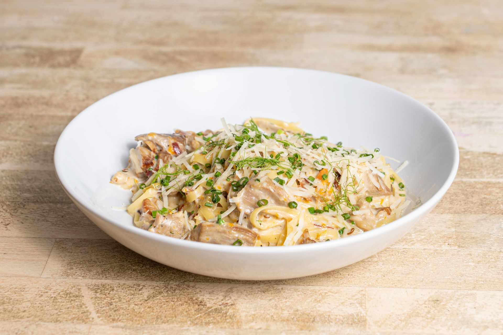A white bowl filled with pasta and cheese on a wooden table.