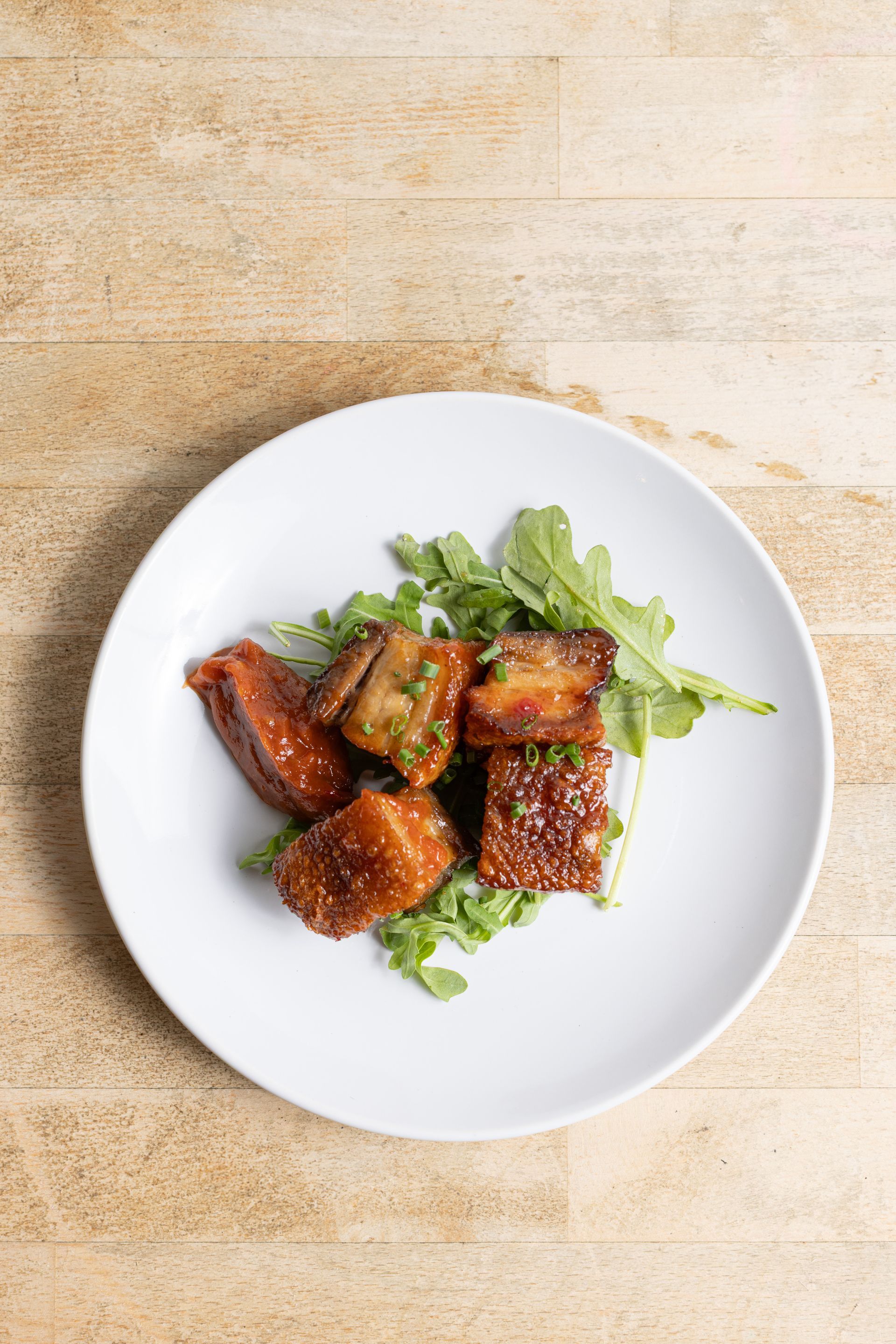 A white plate topped with meat and greens on a wooden table.
