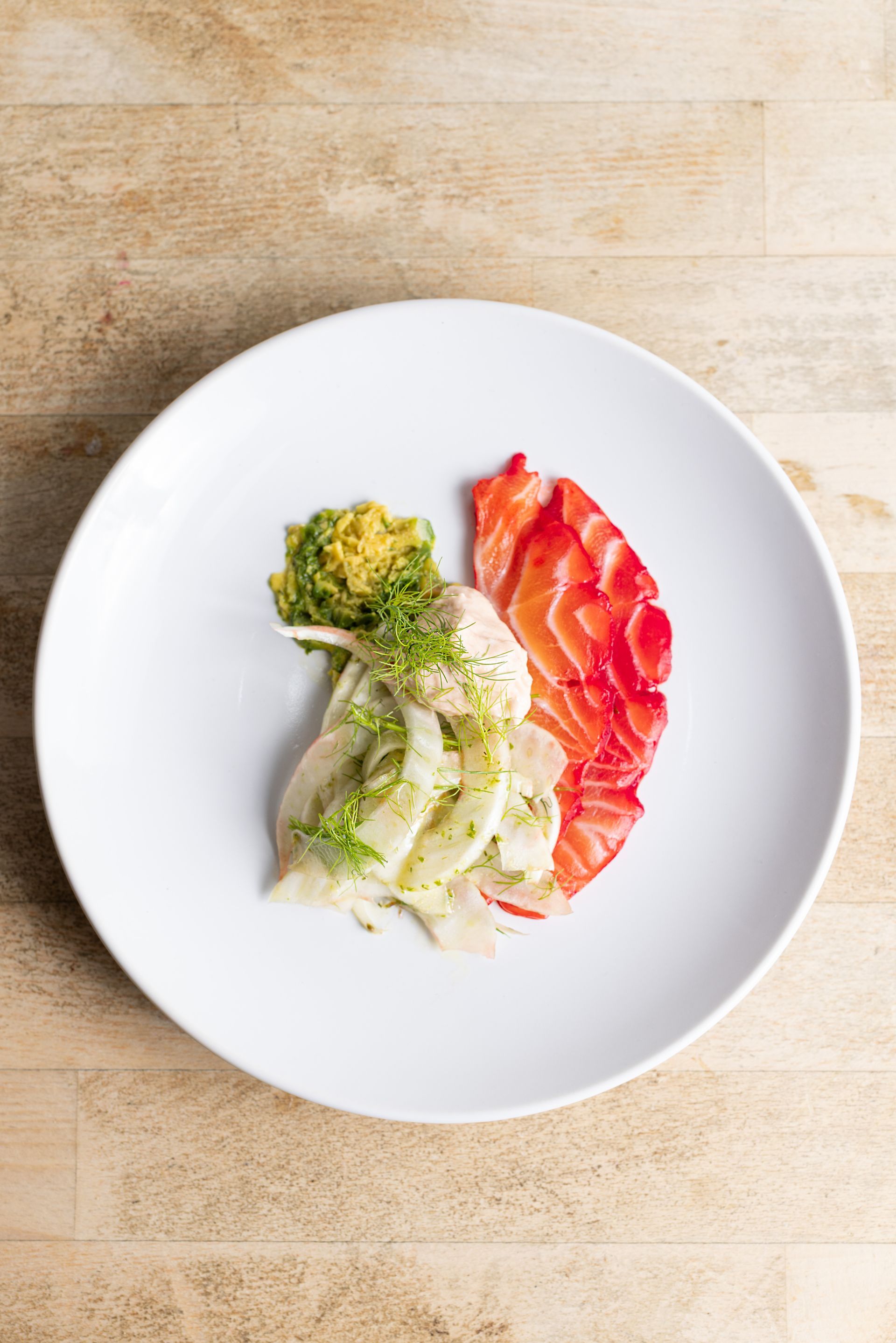 A white plate topped with meat and vegetables on a wooden table.