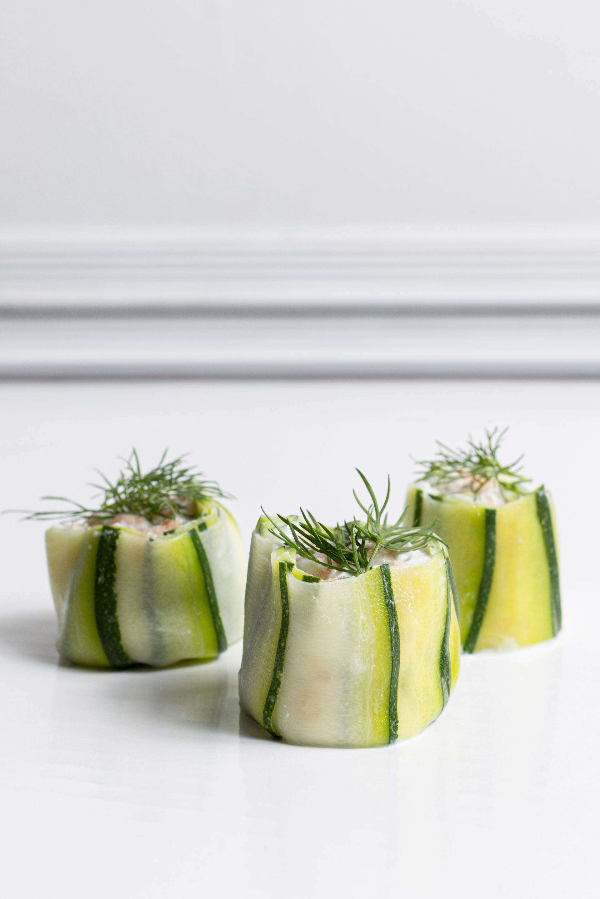 Three zucchini rolls with dill on a white surface.