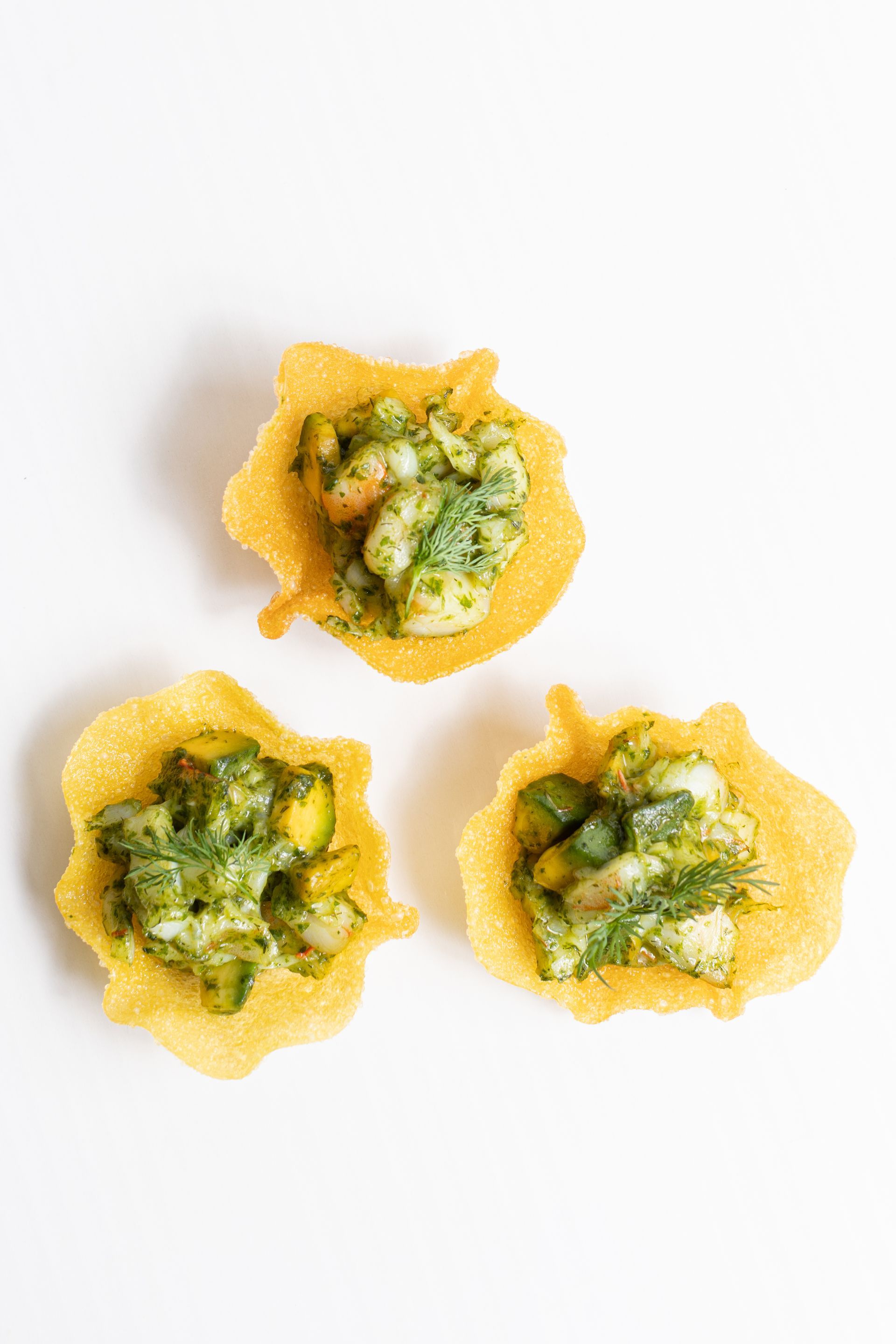 Three tortilla cups filled with guacamole on a white background.