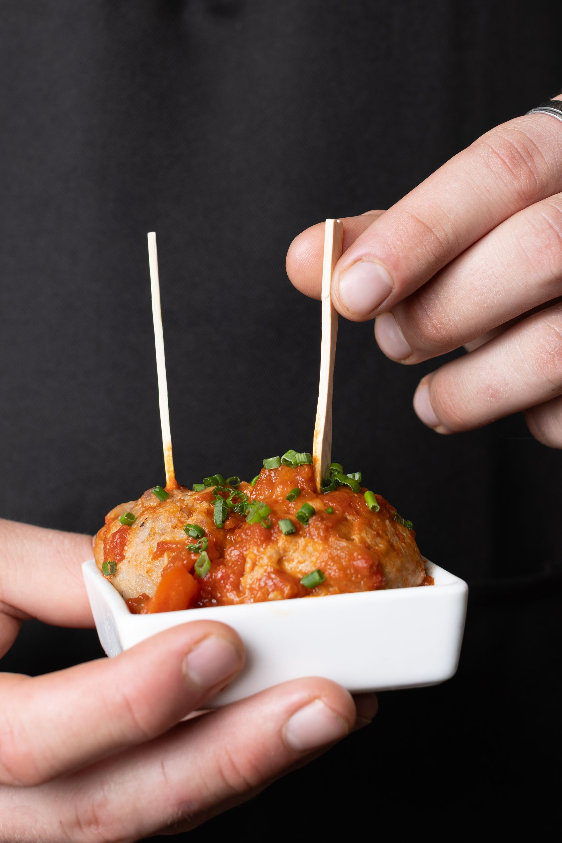 A person is holding a bowl of meatballs with toothpicks in it.