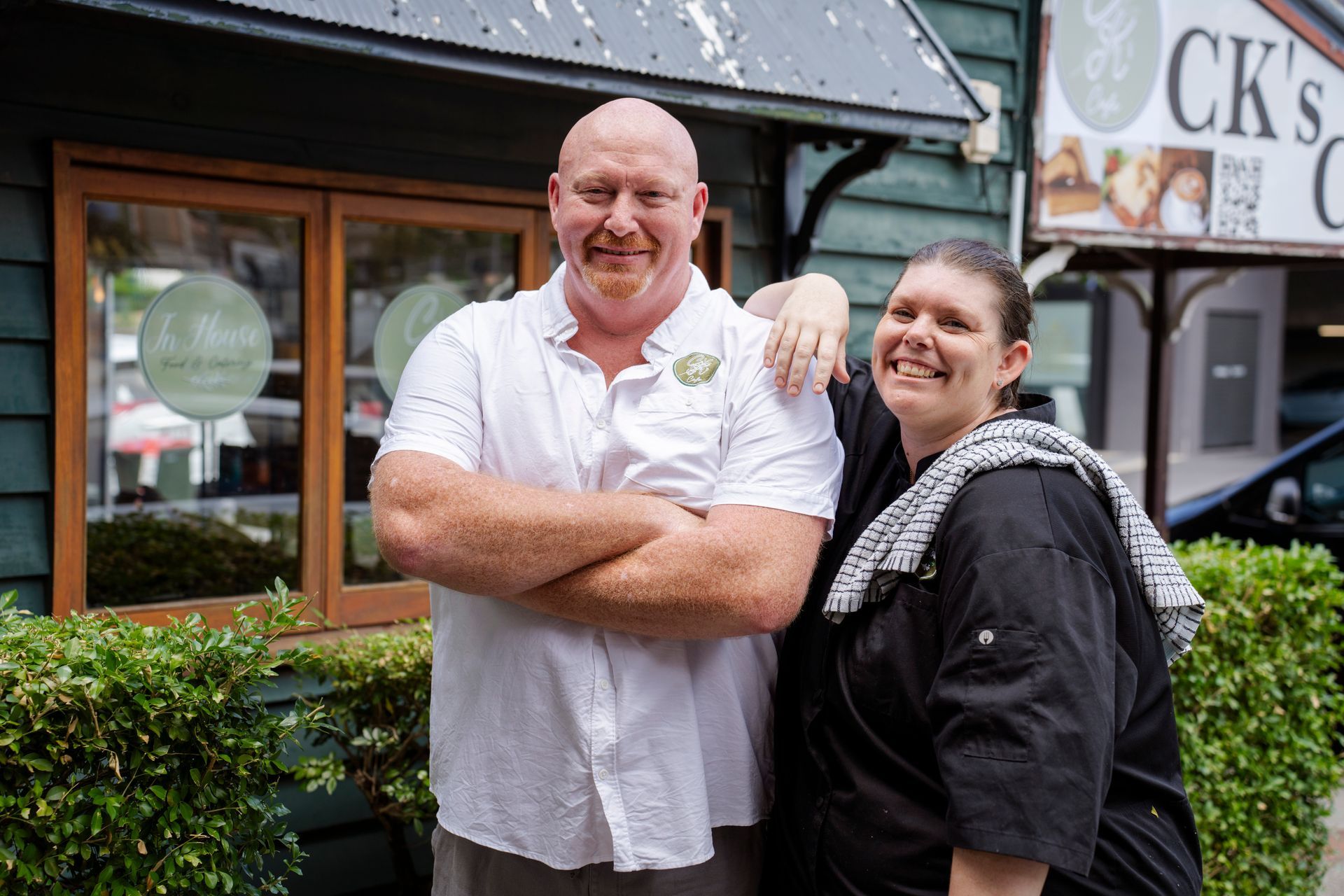 A man and a woman are posing for a picture in front of a restaurant.