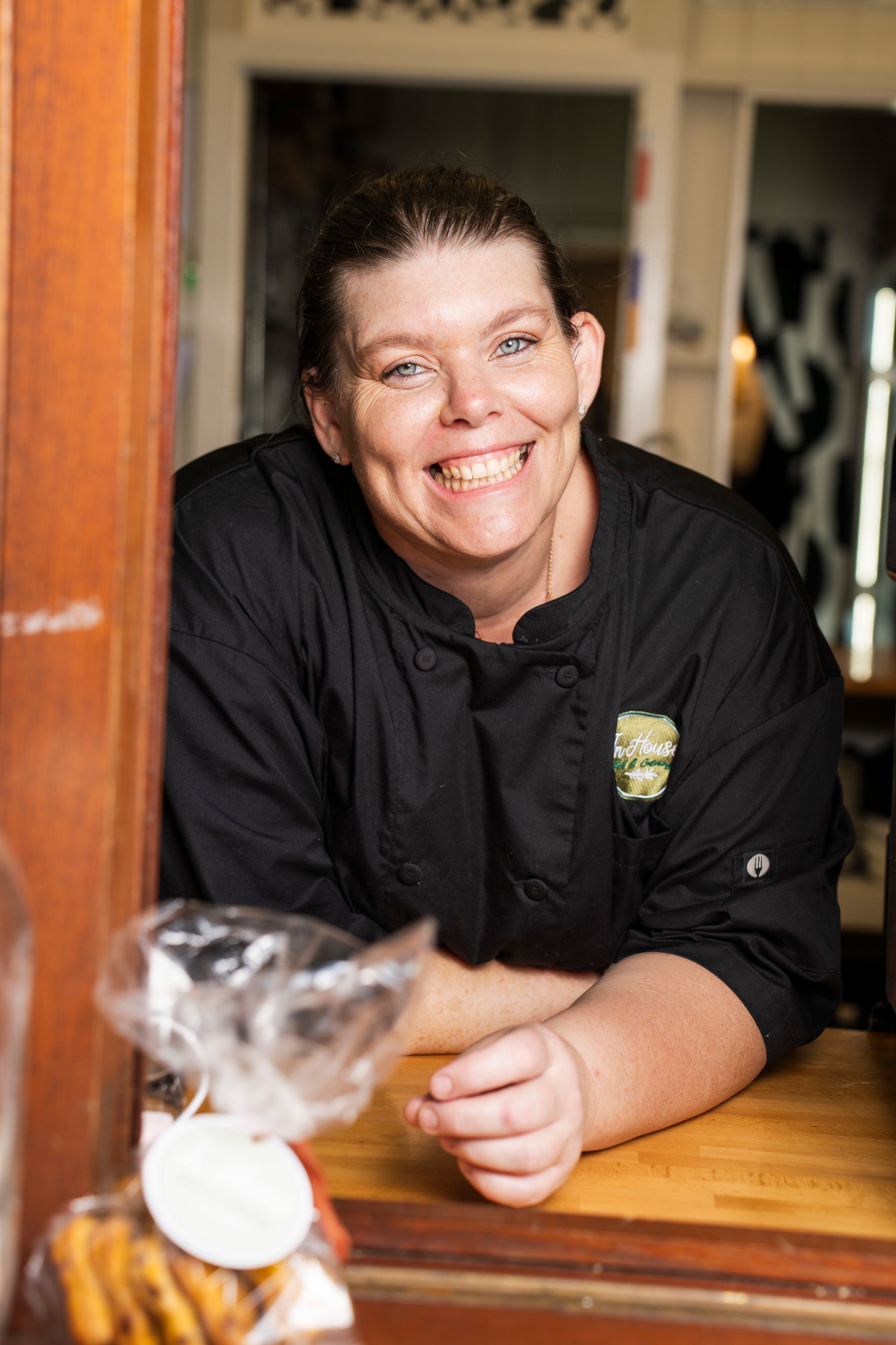 A woman in a chef 's uniform is smiling while sitting at a table.