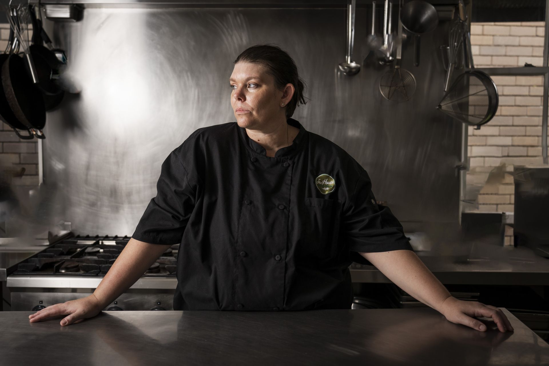 A woman in a chef 's uniform is leaning on a counter in a kitchen.