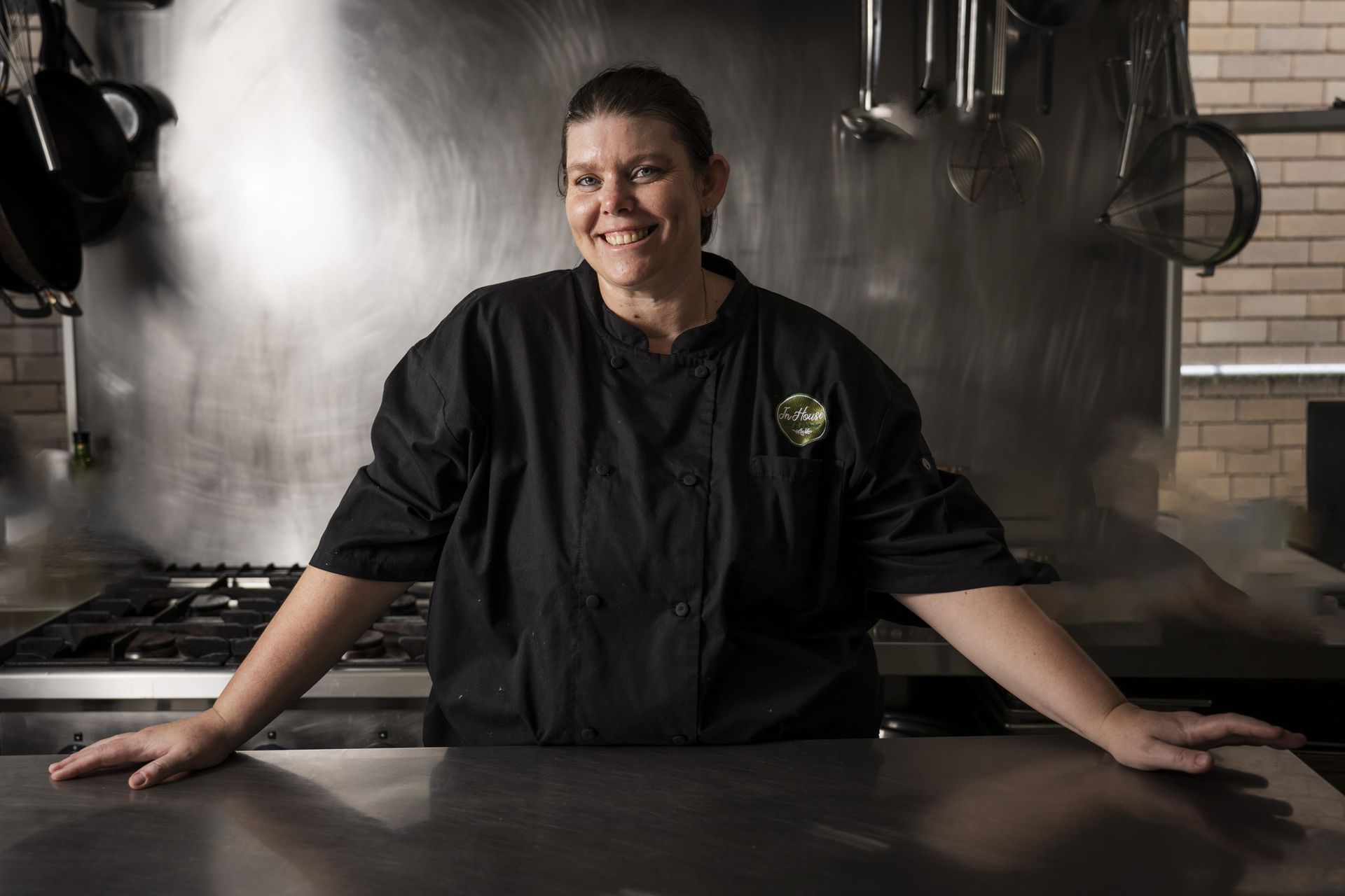 A woman in a chef 's uniform is leaning on a counter in a kitchen