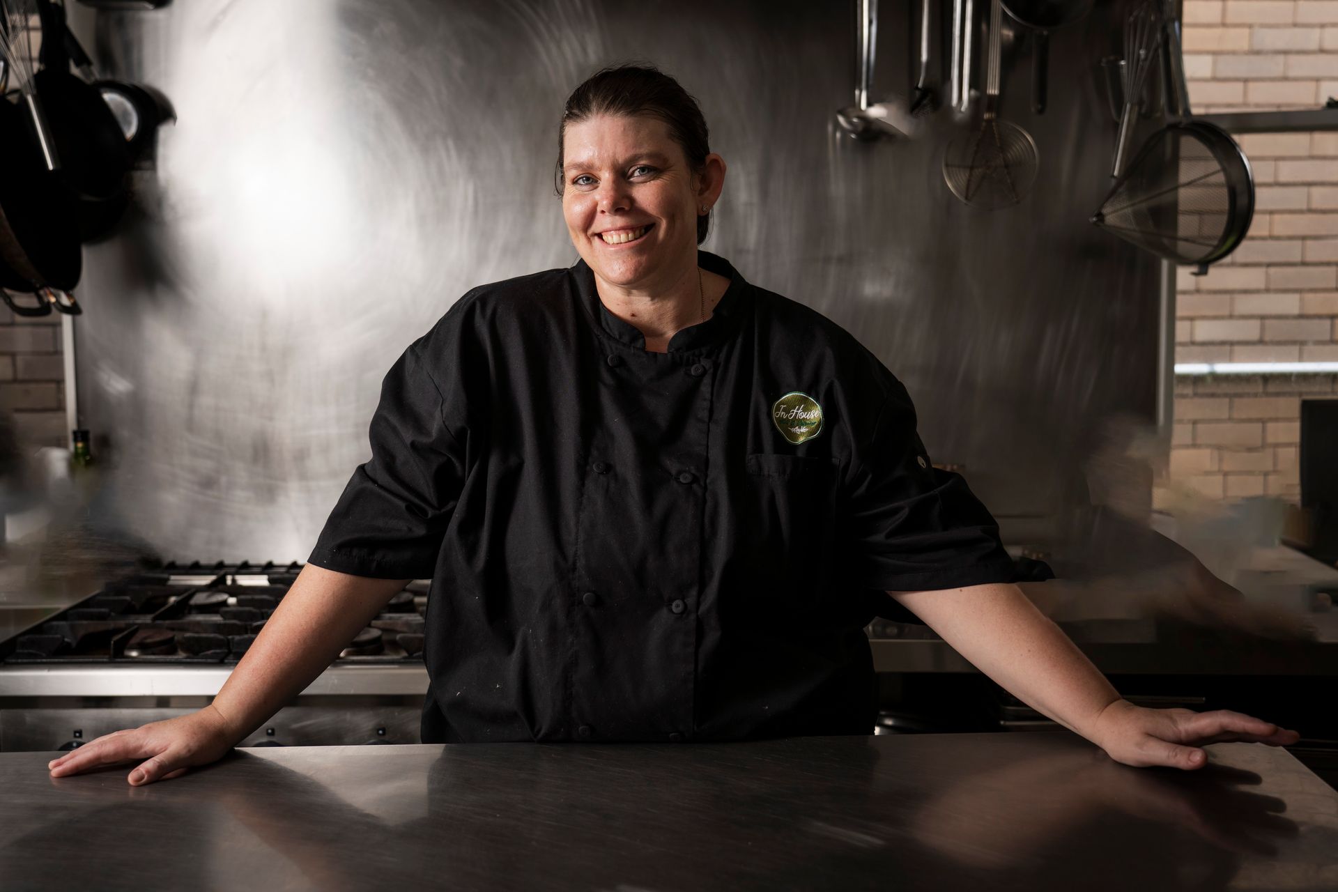 A woman in a chef 's uniform is leaning on a counter in a kitchen.