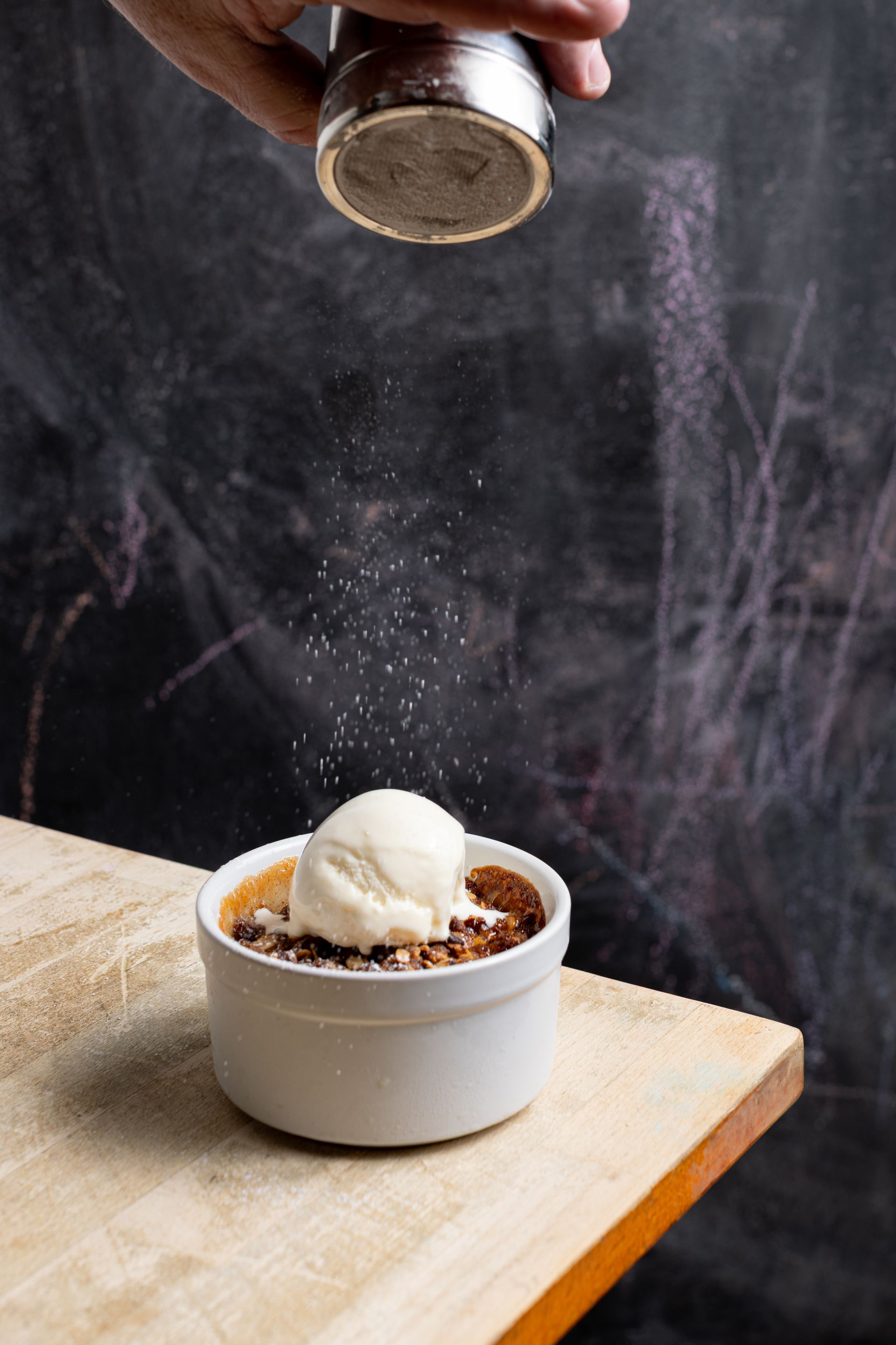 A person is sprinkling sugar on a bowl of food on a table.