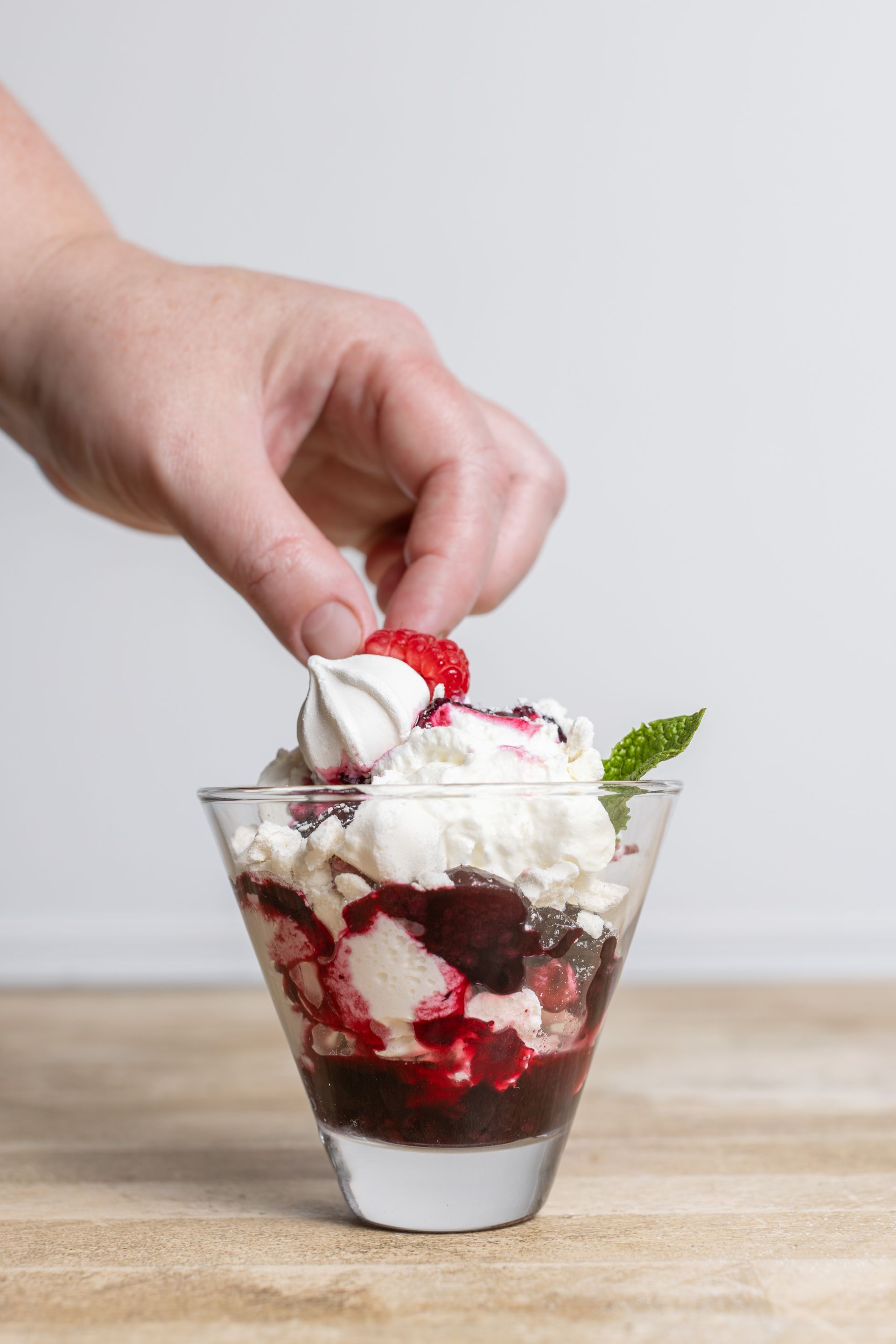 A person is adding whipped cream to a dessert in a glass.
